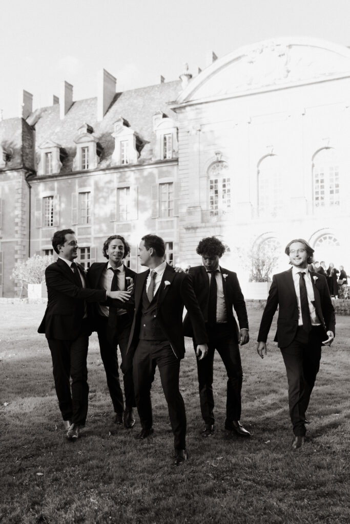 Cinq hommes en costume de marié noir posant avec décontraction sur la pelouse d'un château près de Reims.