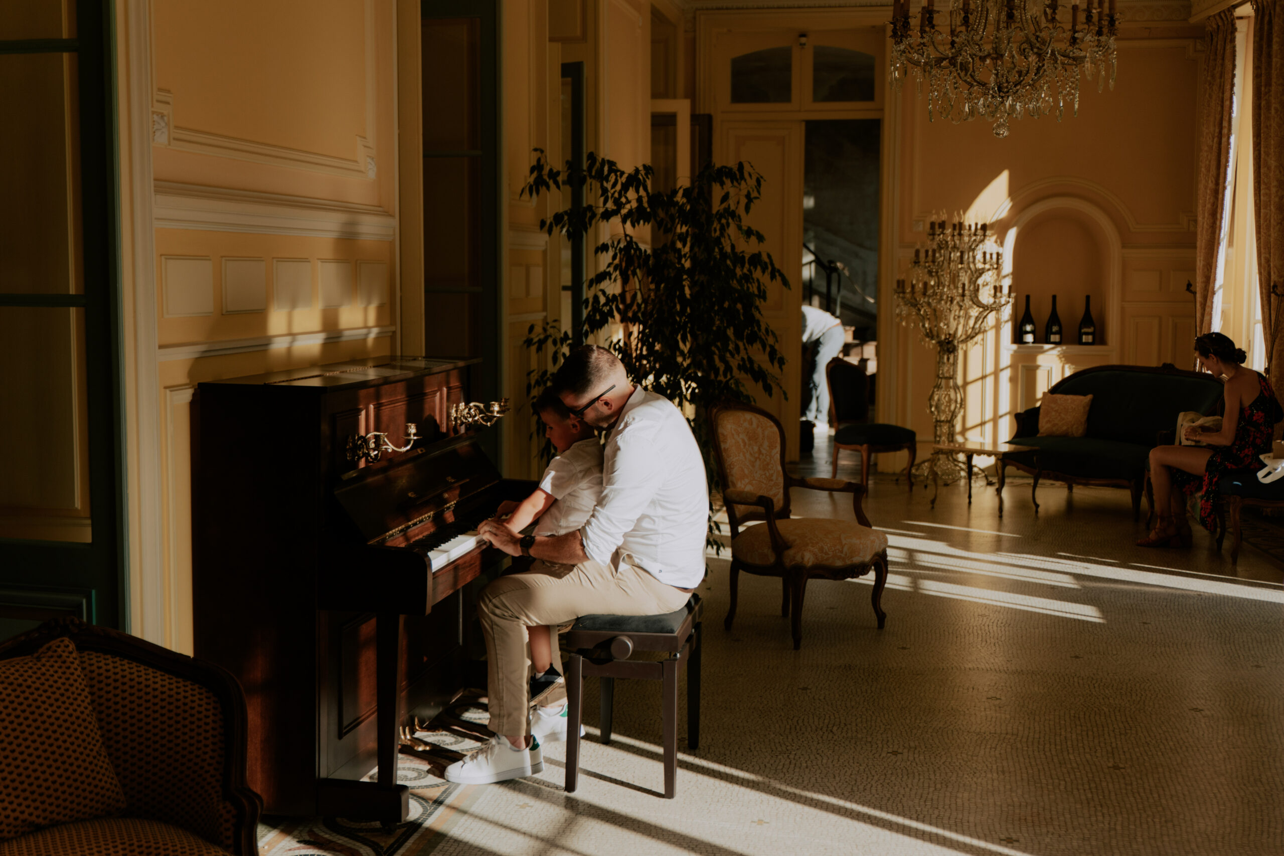 Papa et son fils jouant au piano dans le salon jaune du Château de Droupt-Saint-Basle, lumière naturelle traversante.