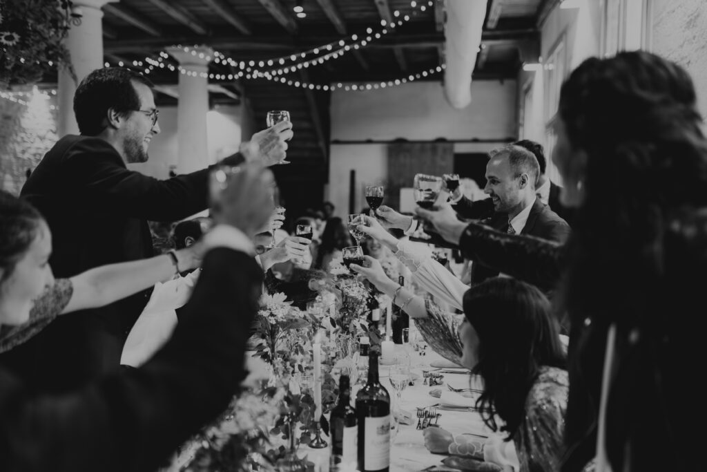 Photo de mariage en noir et blanc avec flou de mouvement montrant la table d'honneur qui trinque en Dordogne. Ambiance festive et artistique de banquet.