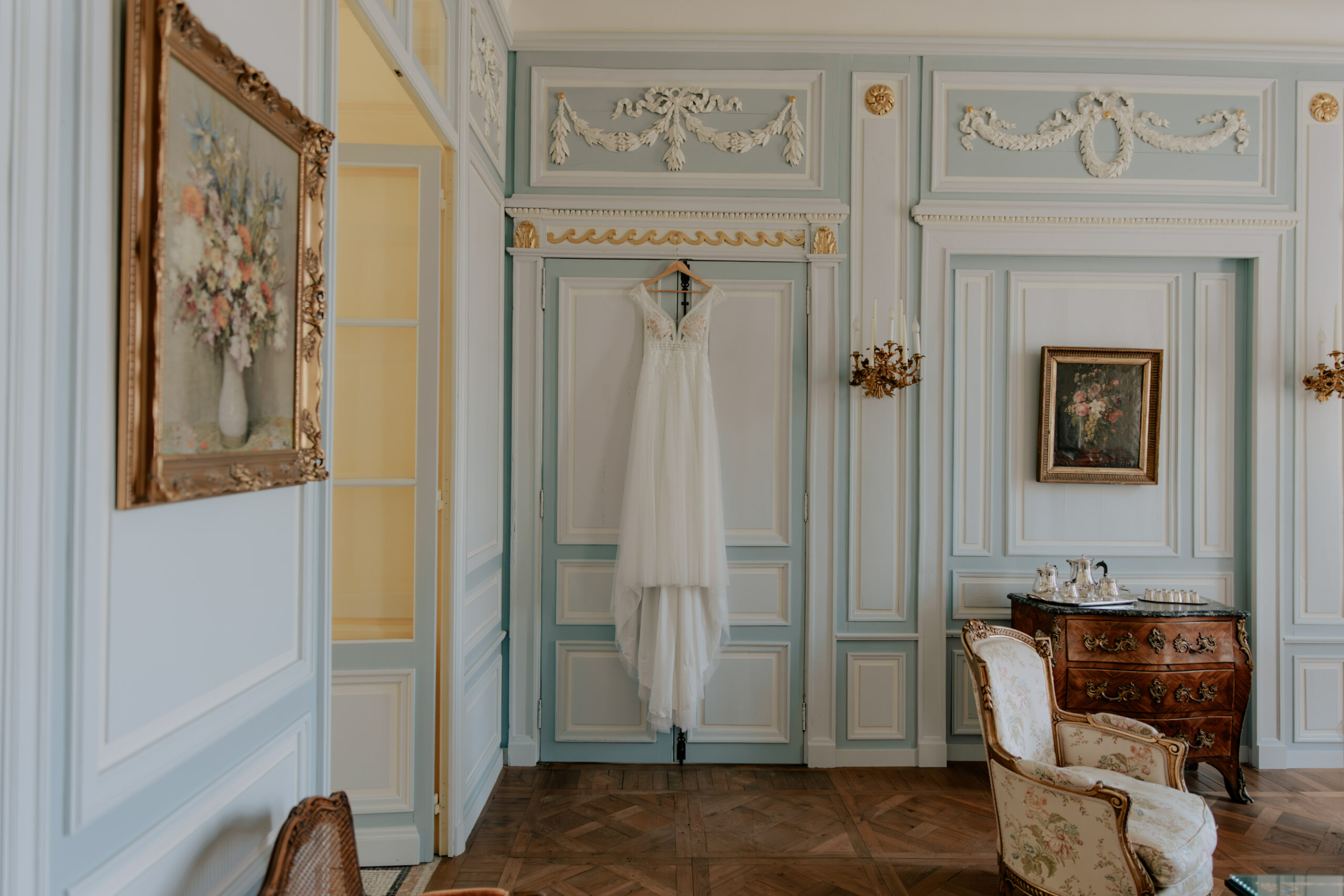 Robe de mariée suspendue dans le salon bleu clair du Château de Droupt avec moulures et dorures.