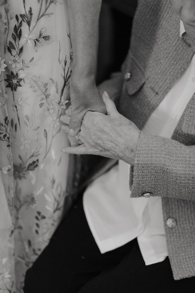 Mains de la grand-mère et de la mère de la mariée entrelacées durant la cérémonie à l'église de Bezannes, photo mariage noir et blanc.