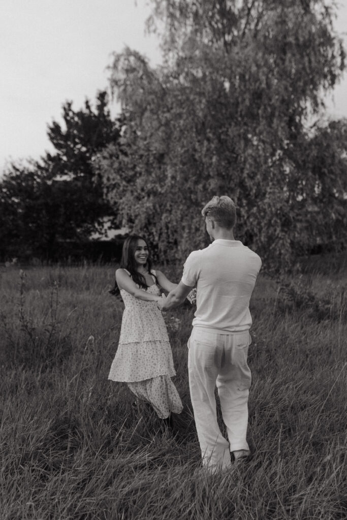 Couple amoureux s'amusant et tournant en rond dans un champ au coucher du soleil à Reims, Champagne-Ardenne. Devant un saule pleureur, photo en noir et blanc.