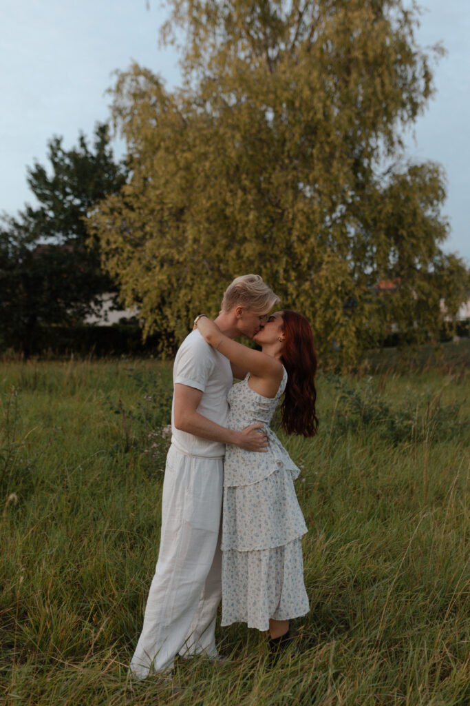 Couple s'embrassant devant un saule pleureur majestueux dans un champ près de Reims lors d'une séance engagement.