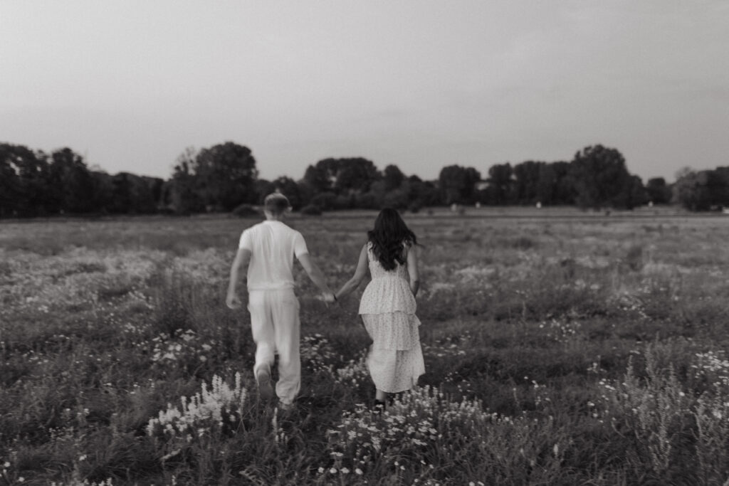 Photographie en noir et blanc d'un couple courant joyeusement dans un champ de fleurs sauvages près de Reims, Champagne-Ardenne.