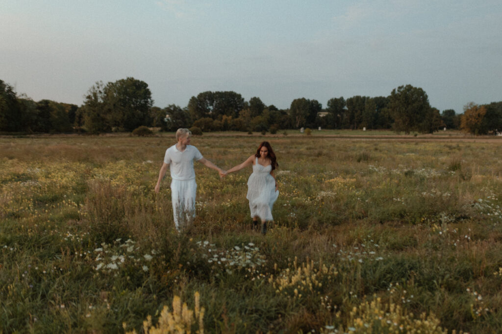 Photographie d'un couple courant joyeusement dans un champ de fleurs sauvages lors d'une séance photo près de Reims, Champagne-Ardenne.