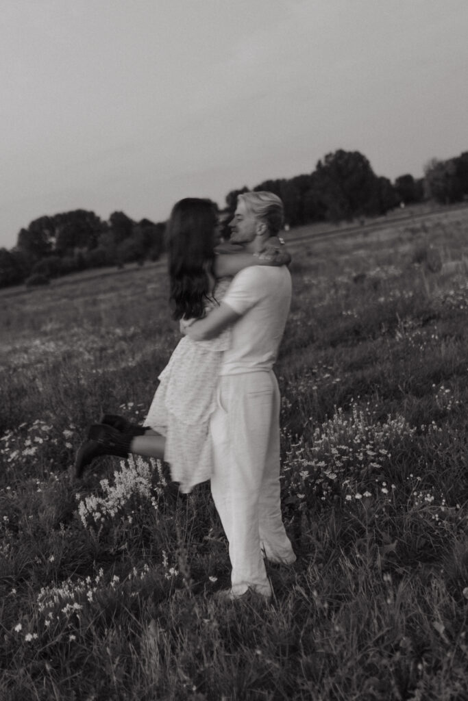 Photographie en noir et blanc d'un couple lors d'une séance photo à la Blue Hour près de Reims, Champagne-Ardenne. L'homme porte sa femme, ils se regardent profondément, avec un flou de mouvement capturant le dynamisme.
