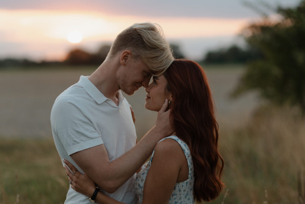 Portrait très rapproché en couleur lors d'une séance engagement à Prunay, près de Reims, au coucher du soleil. Les visages d'un couple se font face, ils se regardent profondément et intensément, entourés de hautes herbes dorées.