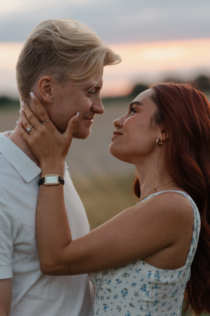 Plan très rapproché d'une femme souriant amoureusement en regardant son compagnon dans les yeux. Portrait réalisé à Prunay, près de Reims, dans un champ de hautes herbes au coucher du soleil.