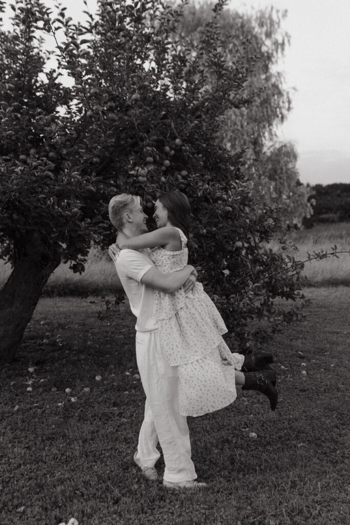 Photographie de couple en noir et blanc, au pied d'un pommier à Prunay. Il la porte dans ses bras et le mouvement est capturé dans cette photo.