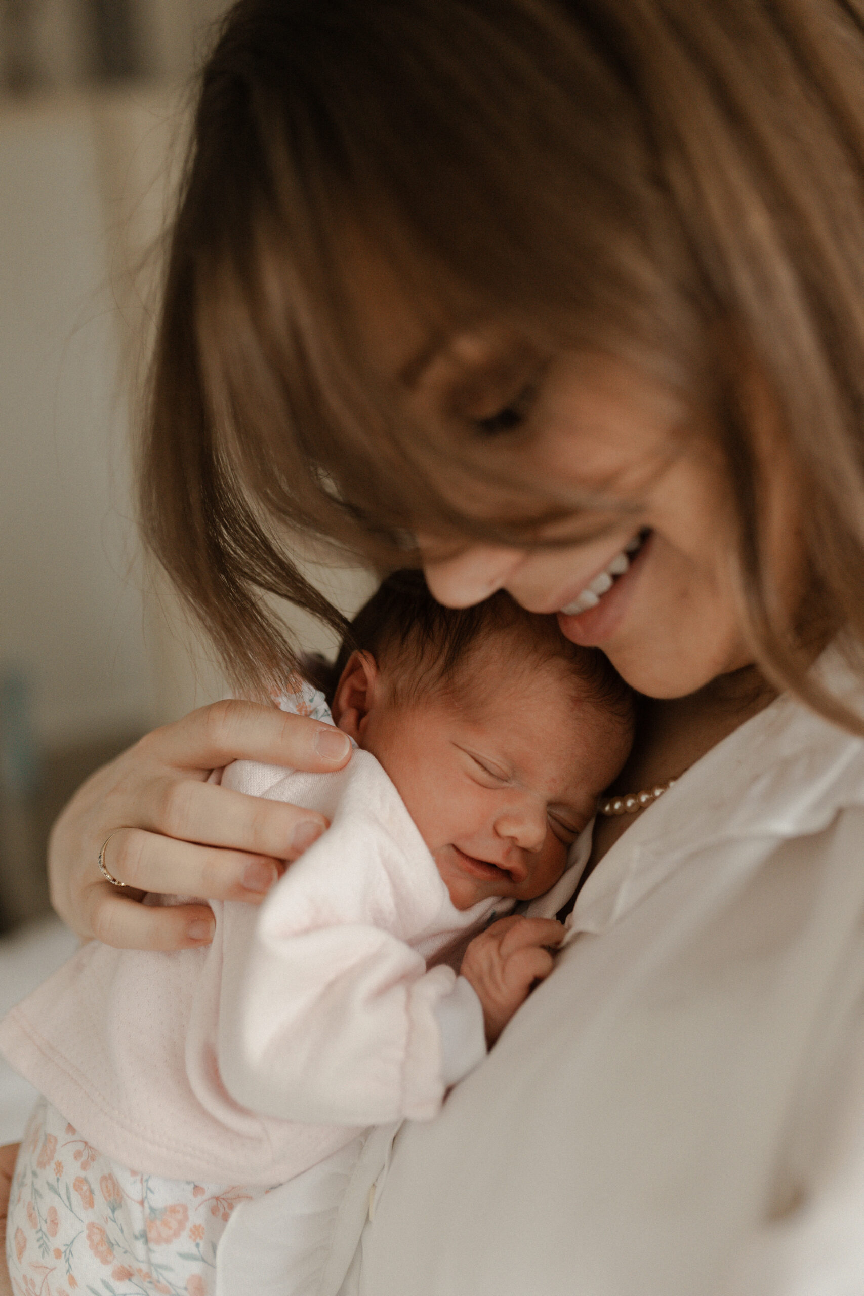 Maman souriante tenant son bébé endormi contre elle, séance photo naissance Reims.