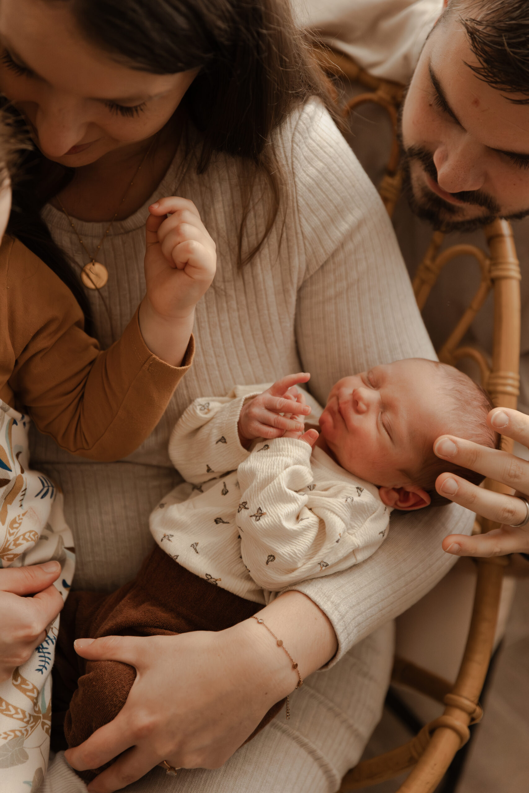 Séance photo nouveau-né en Champagne-Ardenne : bébé dans les bras de maman, papa caressant le visage du nouveau-né avec amour. Portrait de famille chaleureux.