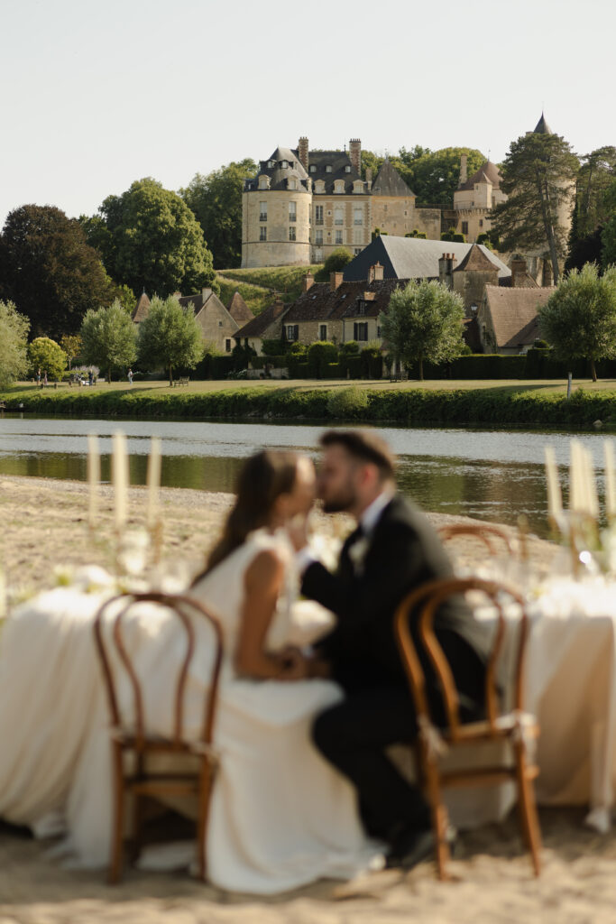 Mariés assis à une table de banquet face à un château médiéval en Bourgogne-Franche-Comté.