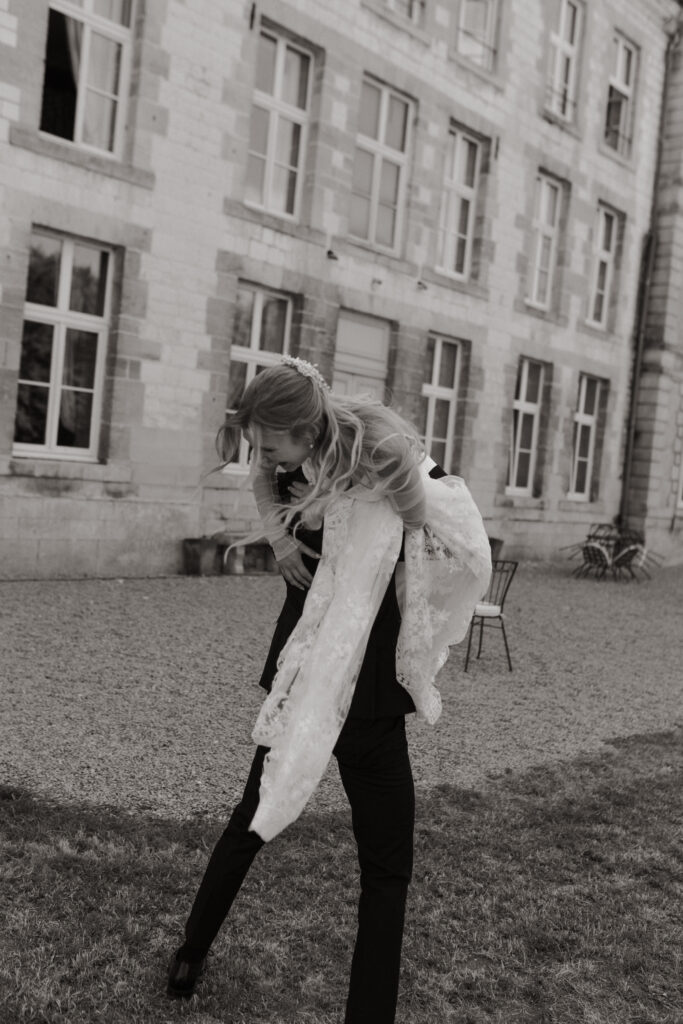 Marié portant sa femme sur son dos devant un château en pierre, mariage Dordogne.