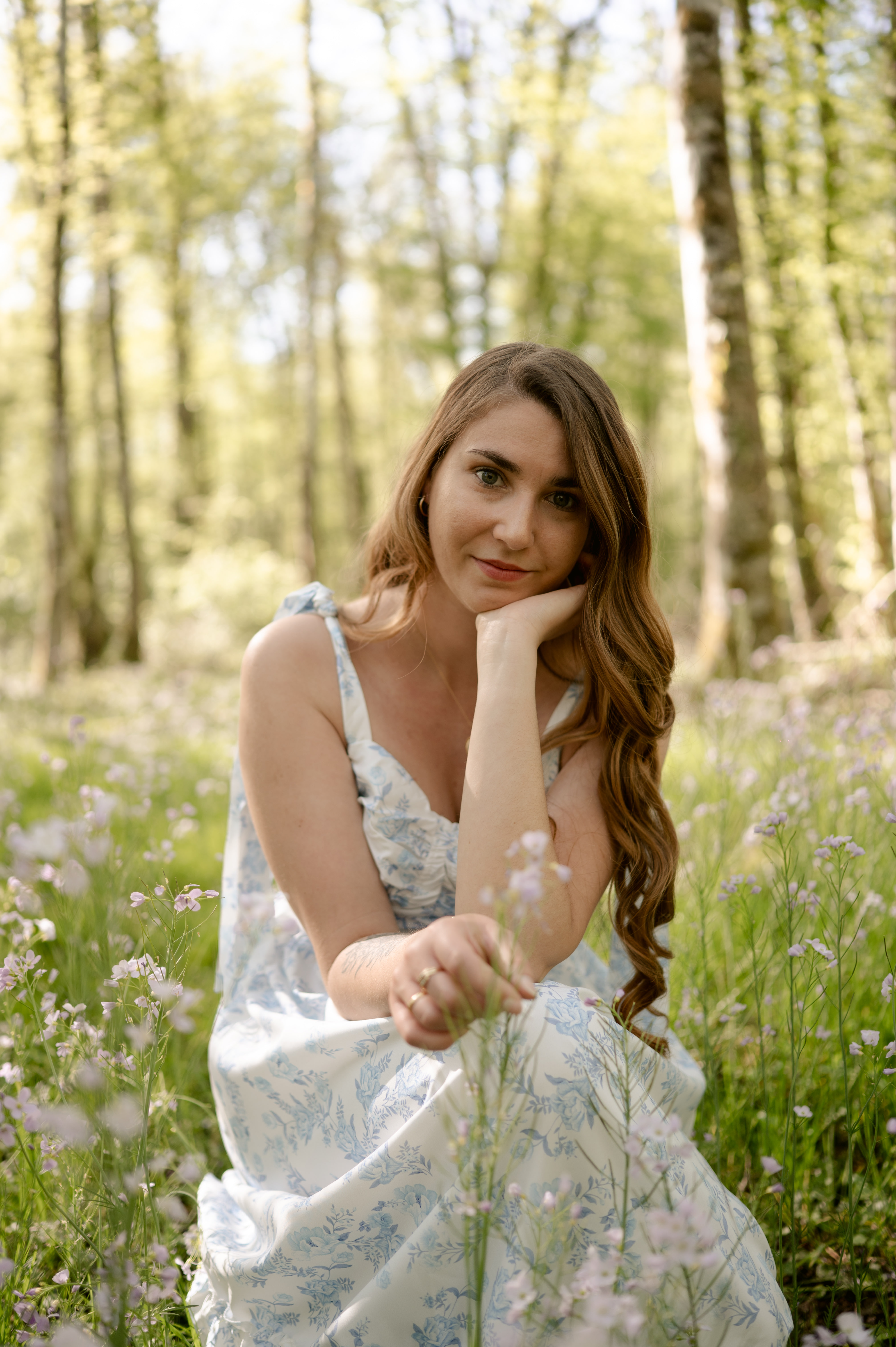 Portrait de votre photographe à Reims en robe toile de Jouy bleue et blanche, assise dans l'herbe au printemps. Style Fine Art et lumineux.