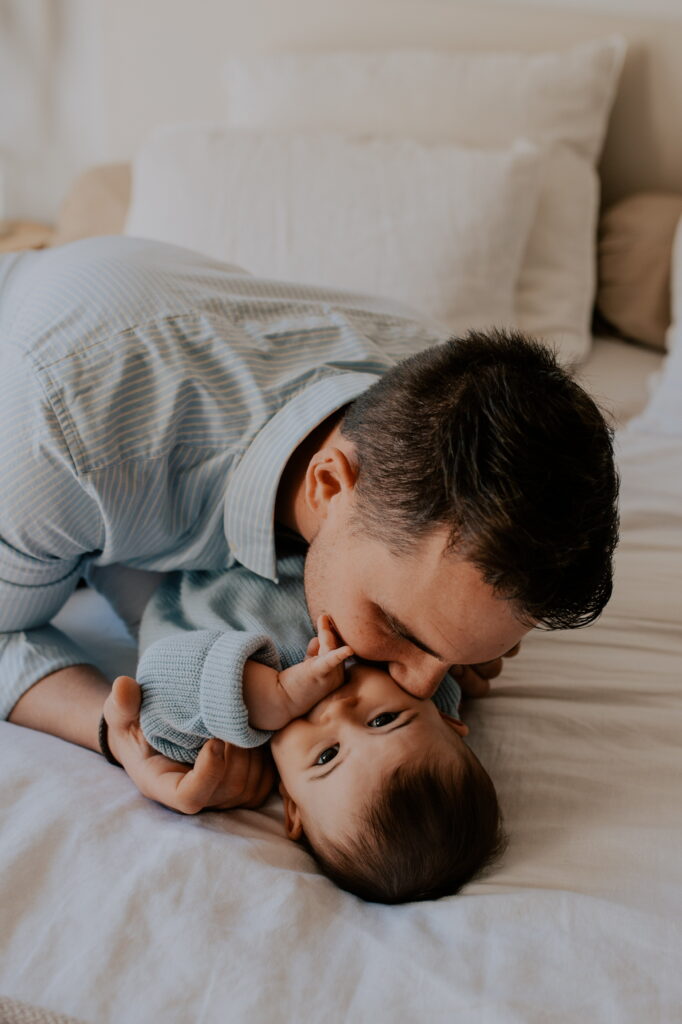 Séance photo famille à domicile près de Reims : un papa joue avec sa petite fille sur un lit. Complicité et rires capturés par votre photographe à Reims.