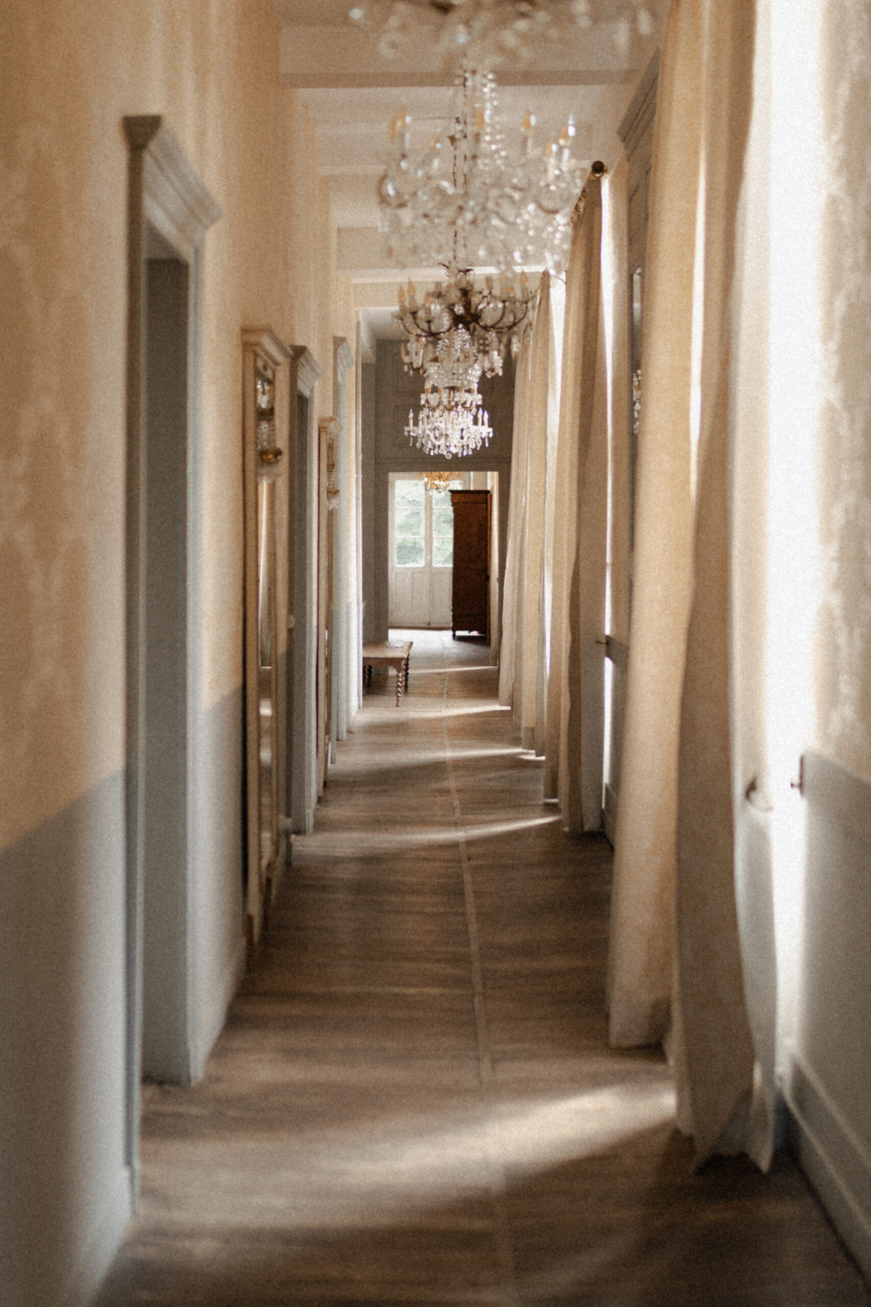 Couloir de l'étage au Château de Mairy avec lustre riche et rideaux de luxe sous le soleil.