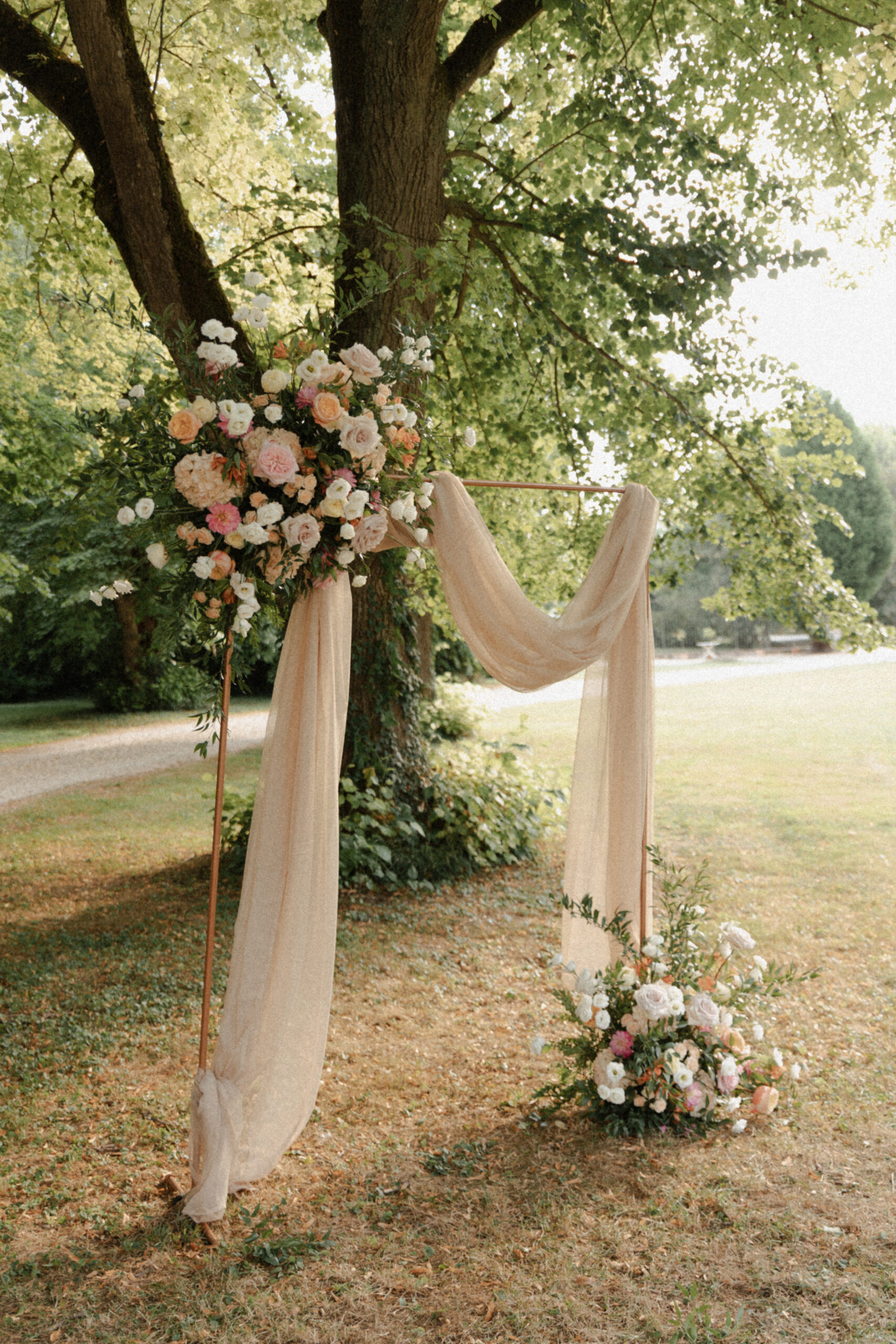 Arche de cérémonie laïque fleurie sous un grand arbre dans le parc du Château de Mairy. Style chic et printanier.