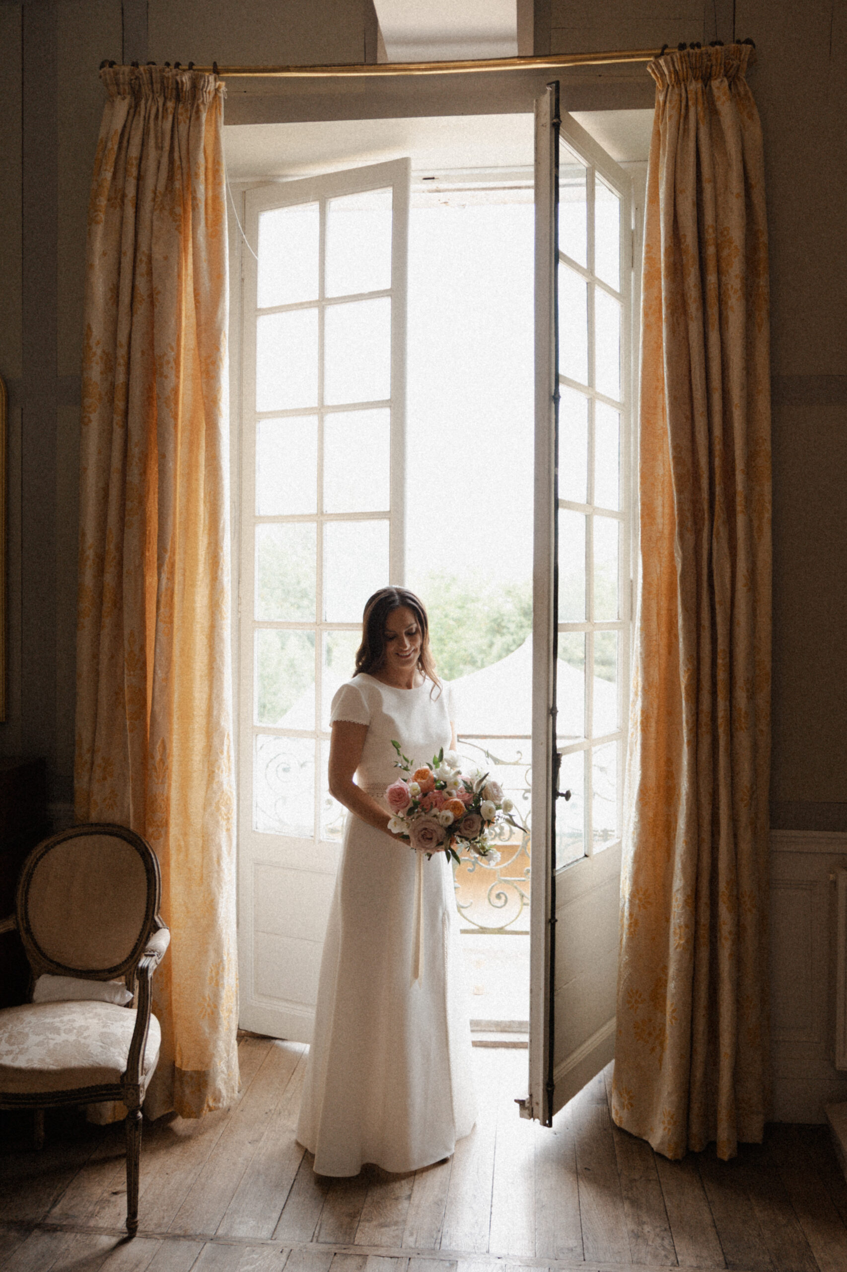 Mariée regardant son bouquet face à la fenêtre en contre-jour au Château de Mairy.