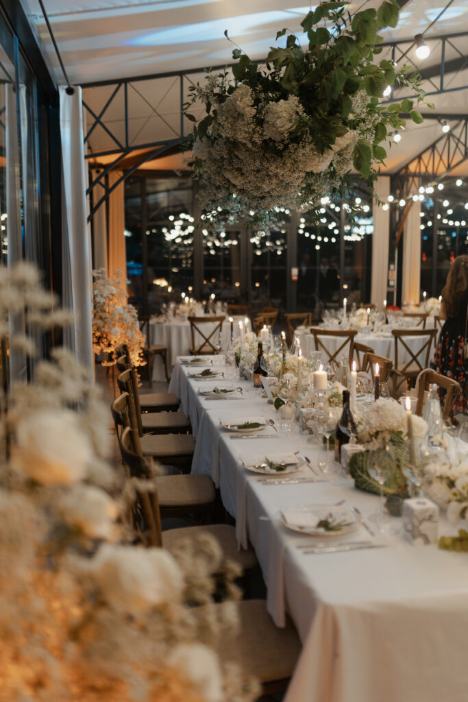 Table d'honneur dans la verrière de Vaugency avec un nuage de fleurs par Safran Lucie, éclairée à la bougie en soirée.