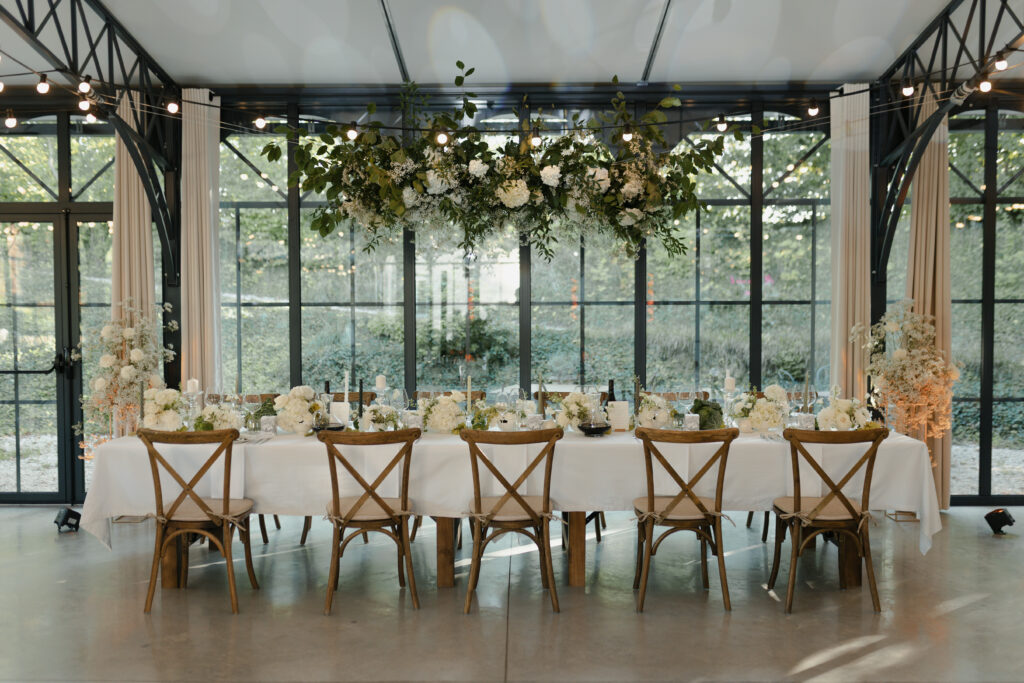 Grande table de banquet fleurie sous une suspension végétale, mariage Domaine de Vaugency.