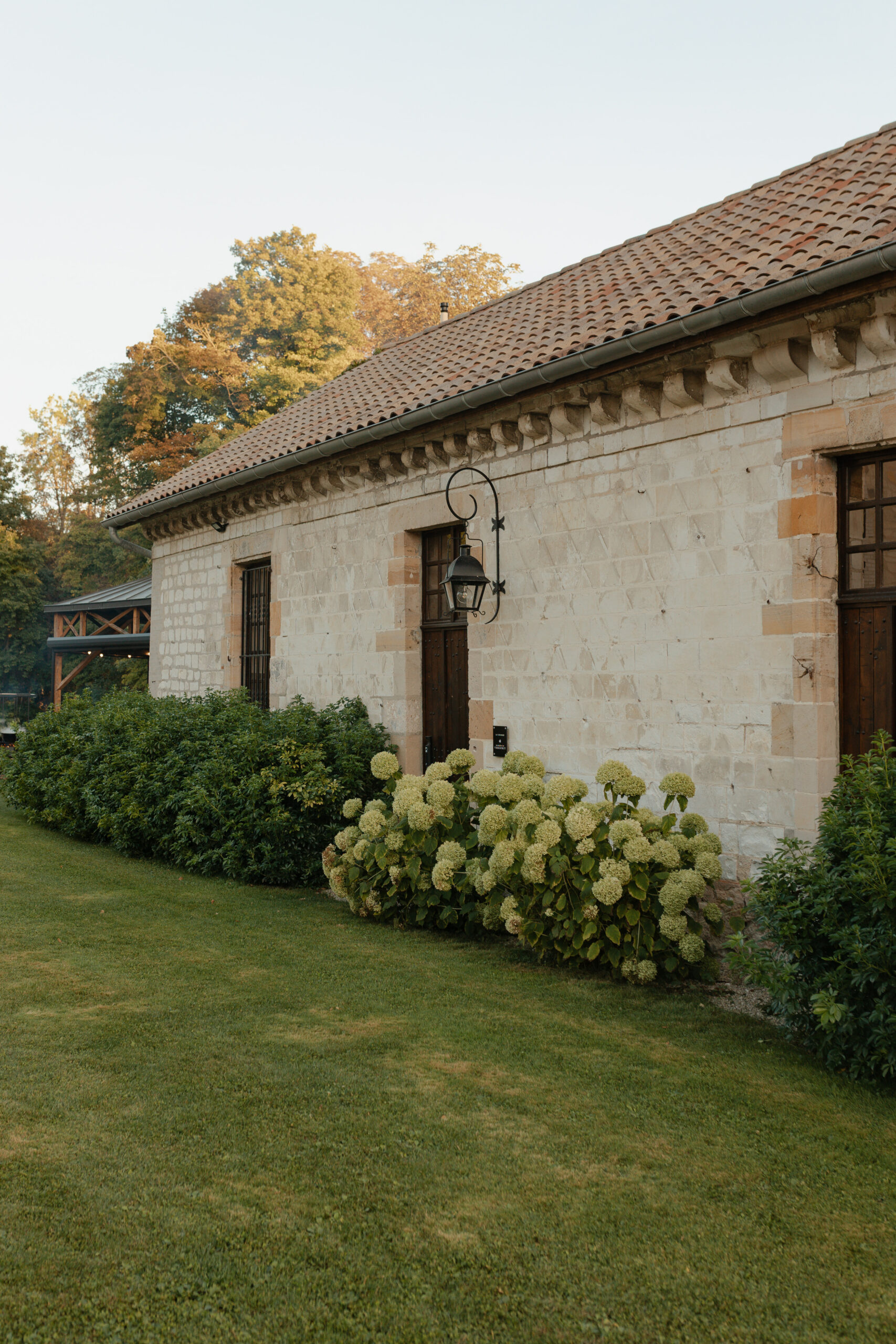 Vue extérieure de la grange du Domaine de Vaugency bordée de buissons d'hortensias en fleurs.