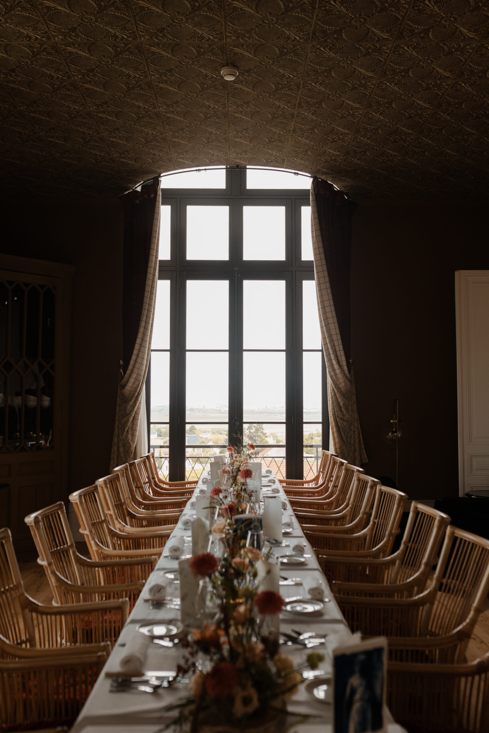 Table de banquet dressée dans la salle de restaurant du Château de Sacy, positionnée devant une fenêtre offrant une vue pittoresque sur le village de Sacy.