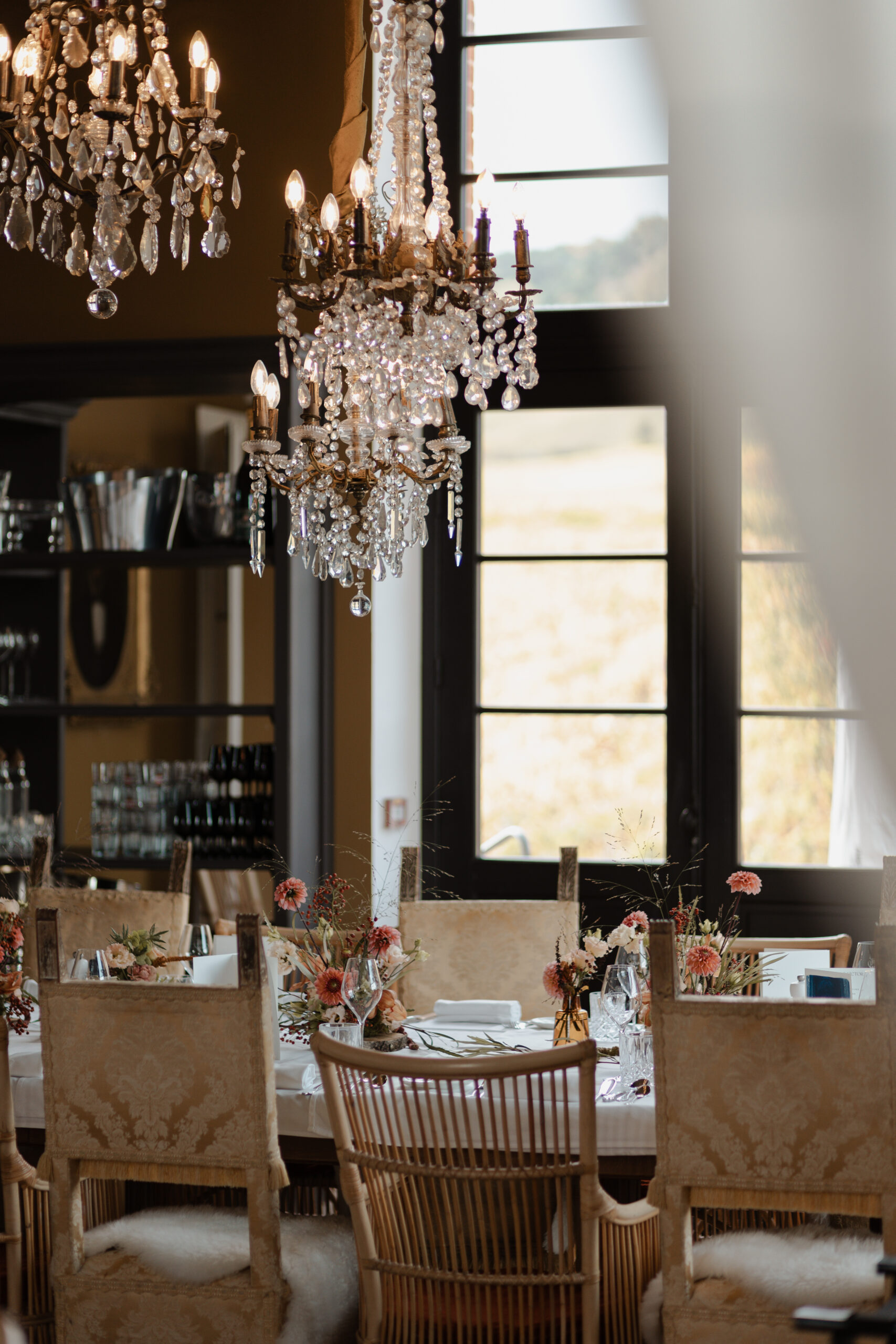 Détail de la salle de réception au Château de Sacy. Les lustres en cristal luxueux surplombent une décoration de table de mariage raffinée avec vaisselle élégante et fleurs.