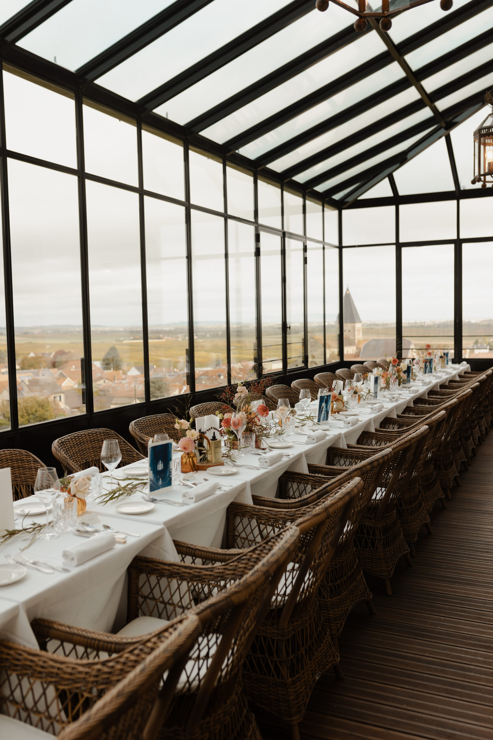 Table de banquet dressée dans la véranda panoramique du Château de Sacy avec une vue imprenable sur le vignoble champenois.