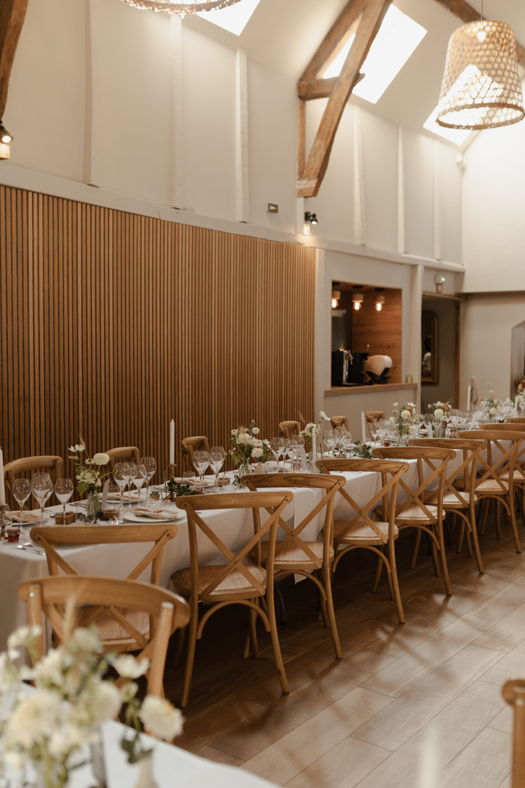 Alignement de chaises de mariage dressées dans la salle de réception du Domaine de la Closeraie. Vaisselle moderne, verres étincelants et centres de table fleuris sous une lumière naturelle douce.