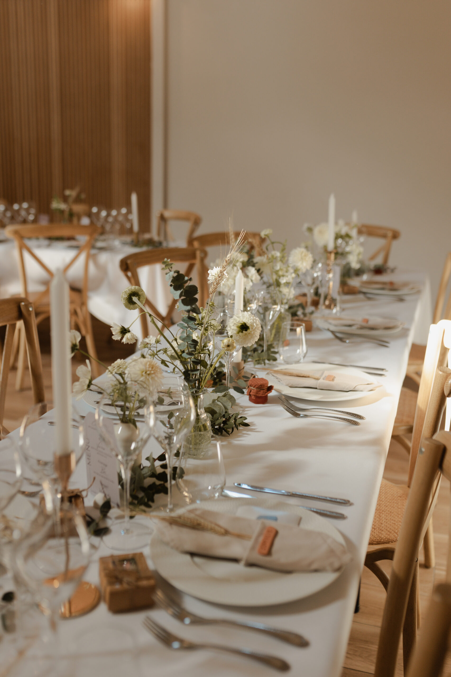 Photographie de détail en couleur au Domaine de La Closeraie. Un rayon de soleil illumine les compositions florales d'une table d'honneur de mariage, créant une ambiance chaleureuse et romantique près de Reims, en Champagne.
