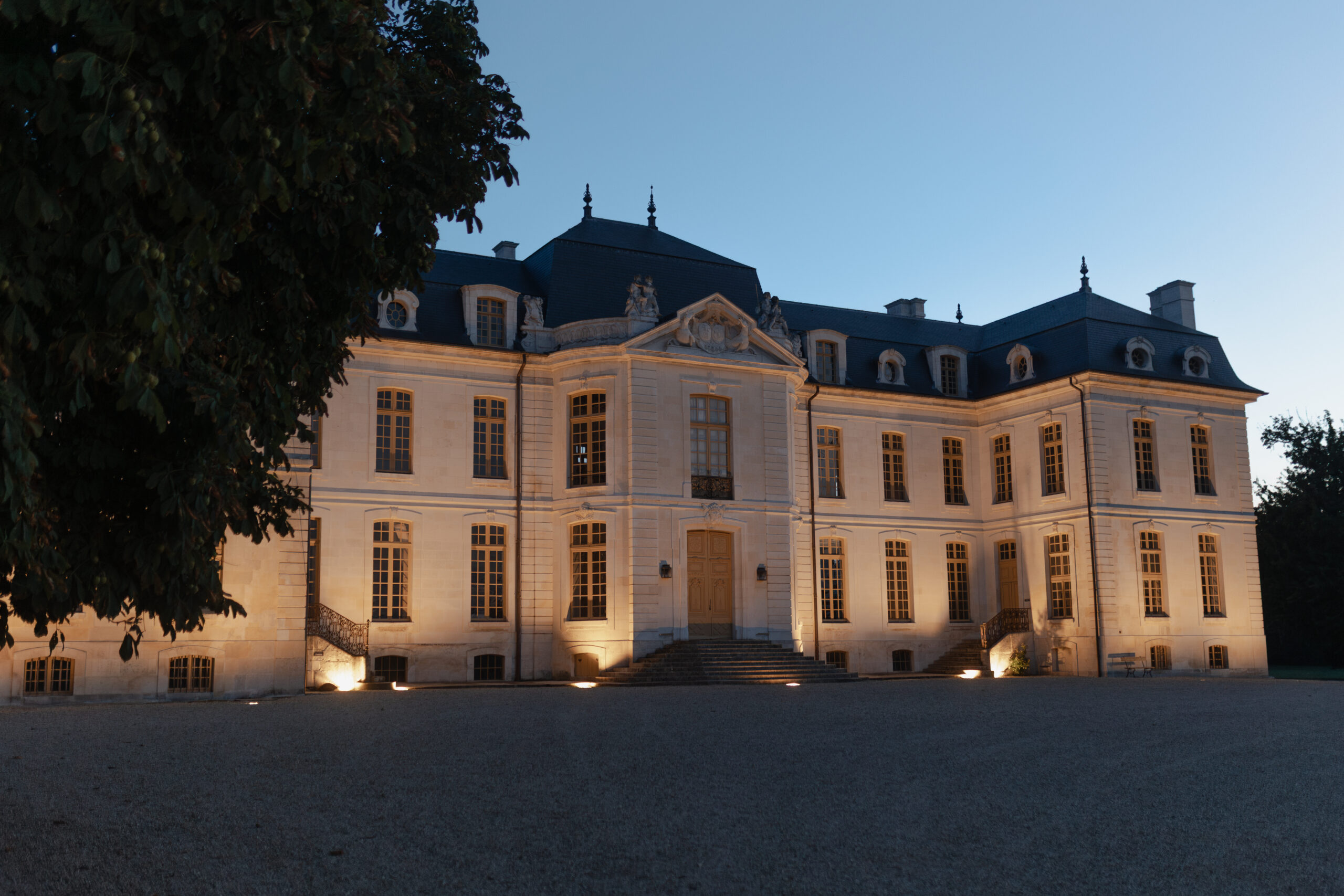 Façade avant du Château de Vaux éclairée à l'heure bleue, à la nuit tombante.