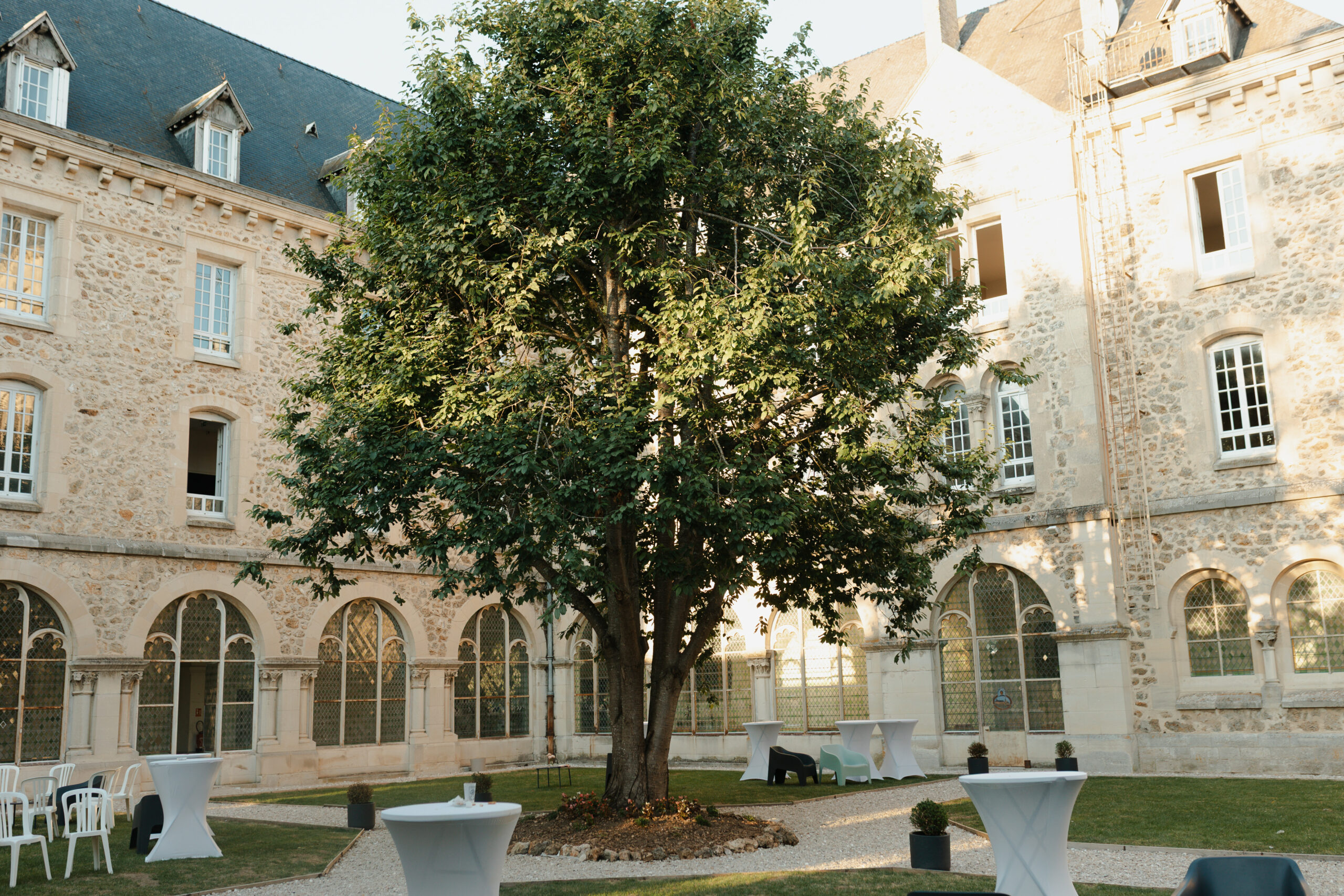 Cour du cloître au Prieuré de Binson avec un bel arbre apportant de l'ombre pour le cocktail de mariage.