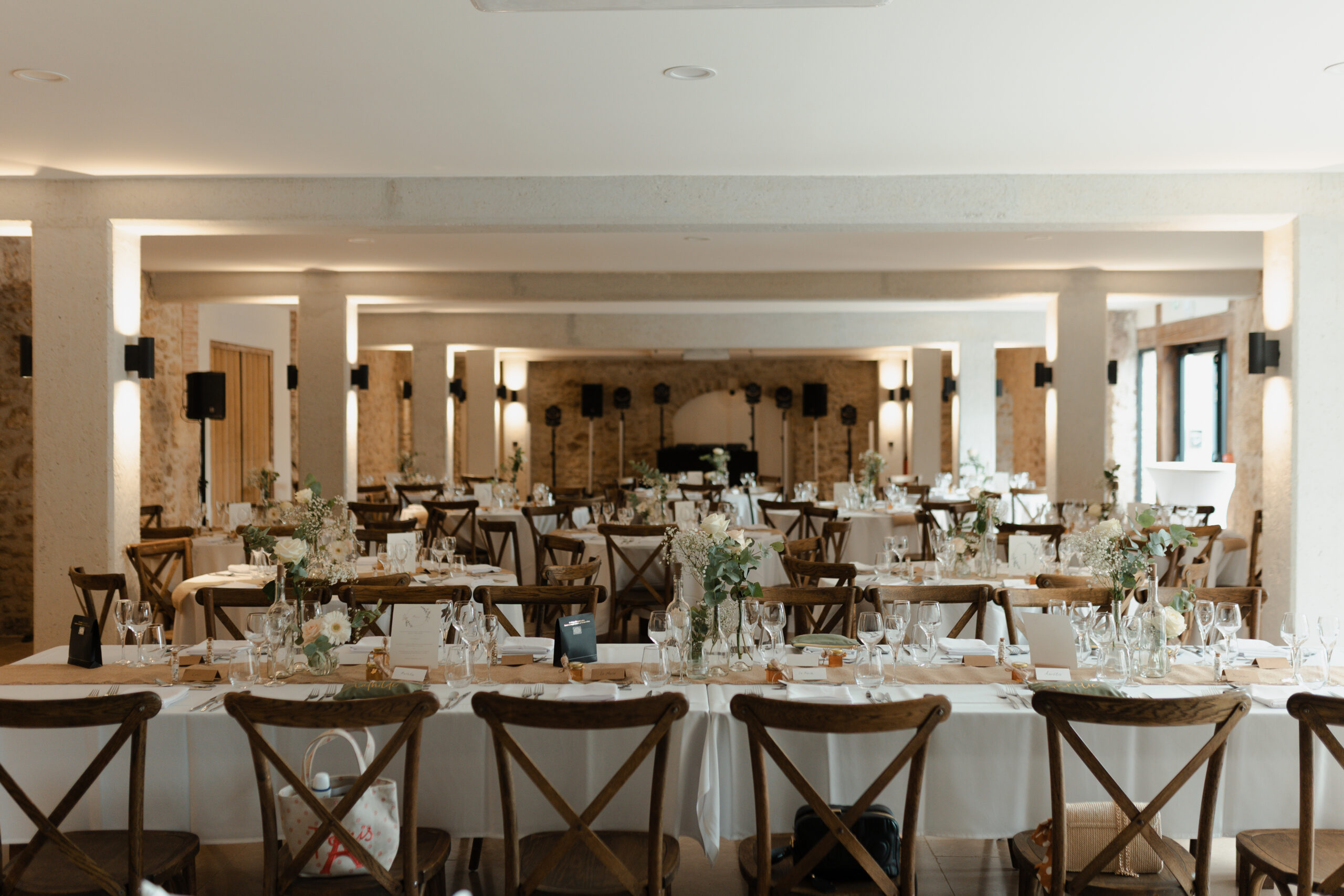 Table d'honneur de mariage au premier plan dans la salle de réception de La Farm. Décoration blanche et naturelle.