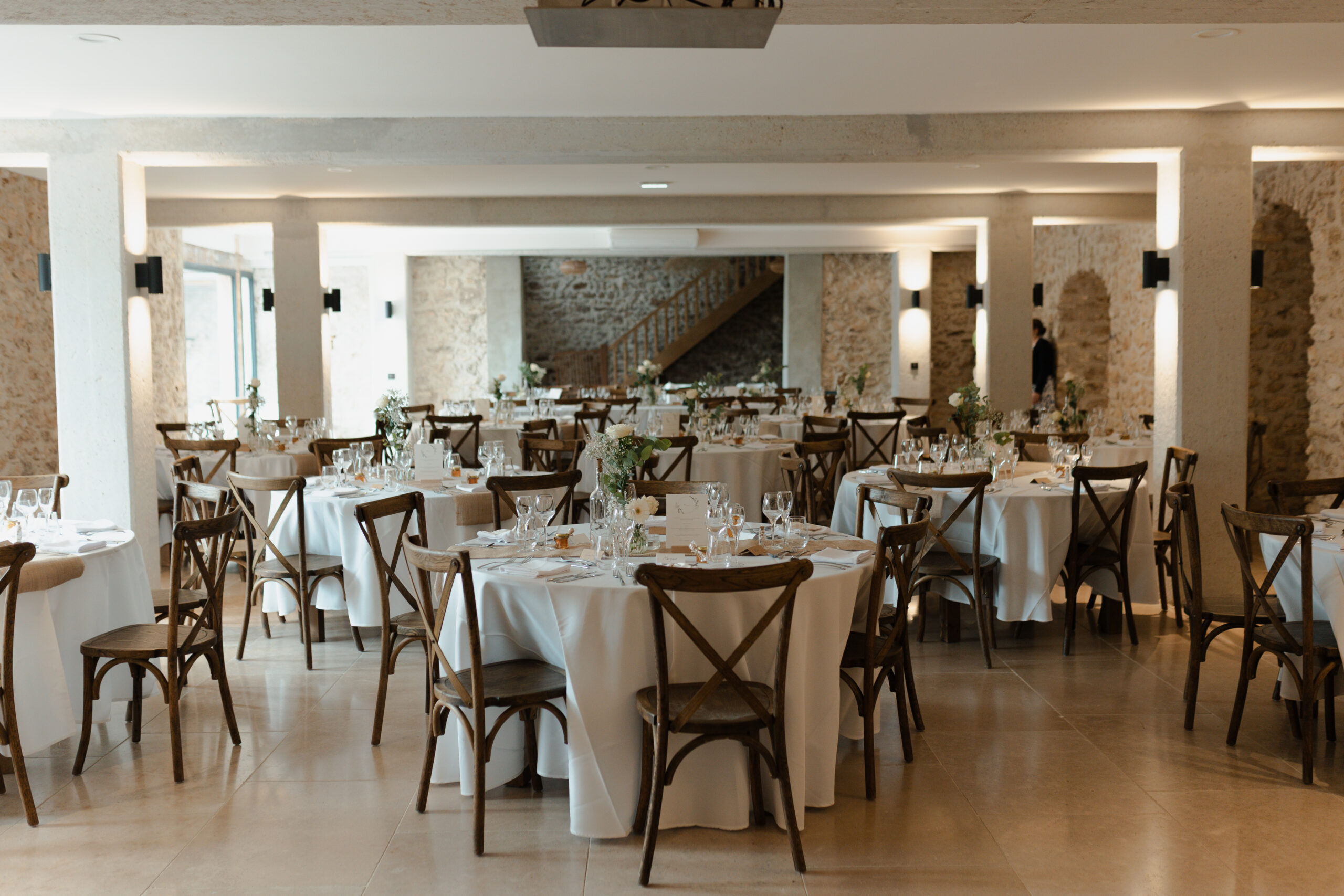 Intérieur de la salle du domaine La Farm décorée sur un thème blanc et naturel. Murs en pierre apparente et poutres blanches.