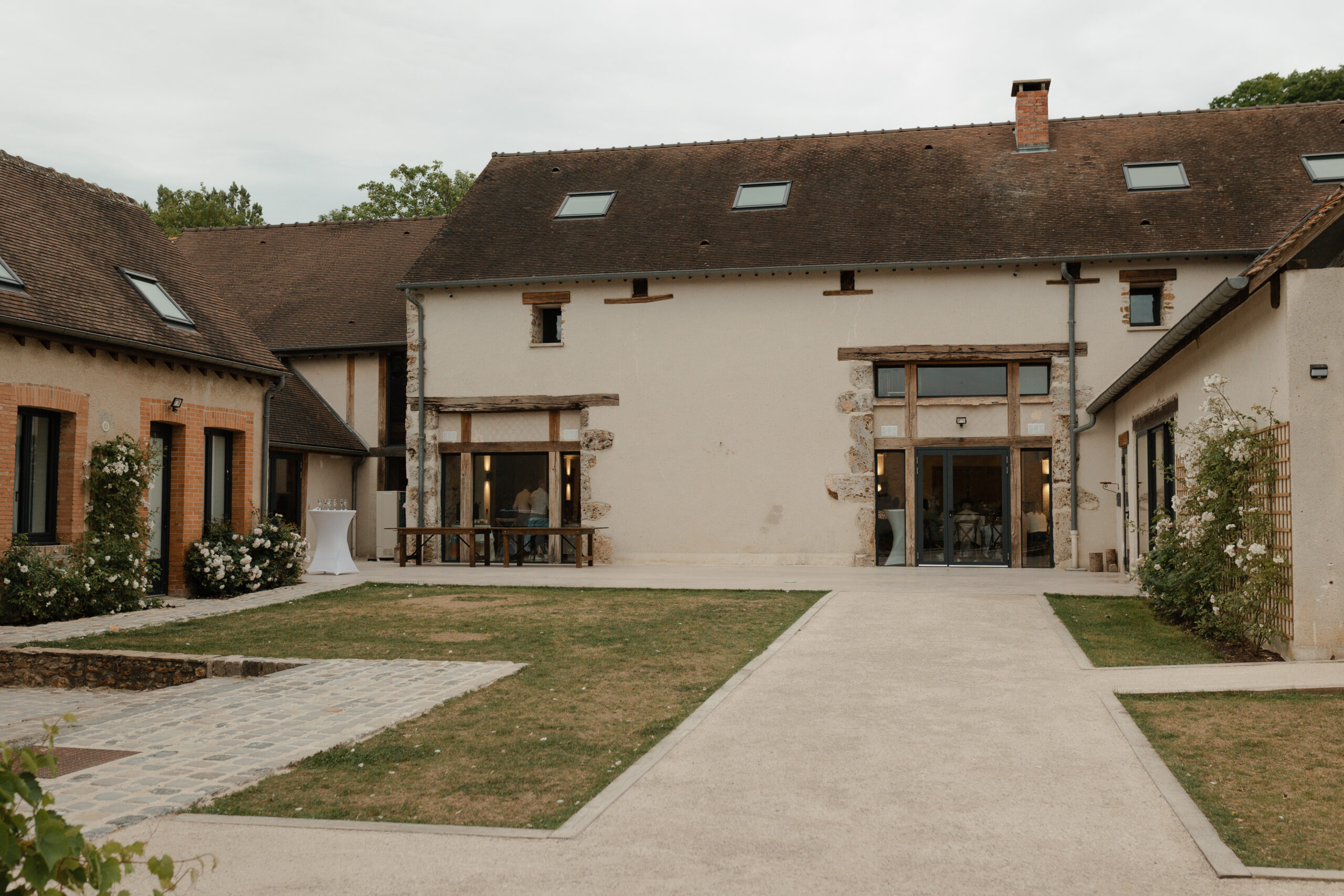 Façade d'une des bâtisses du domaine La Farm entourée de buissons fleuris, domaine mariage Reims.