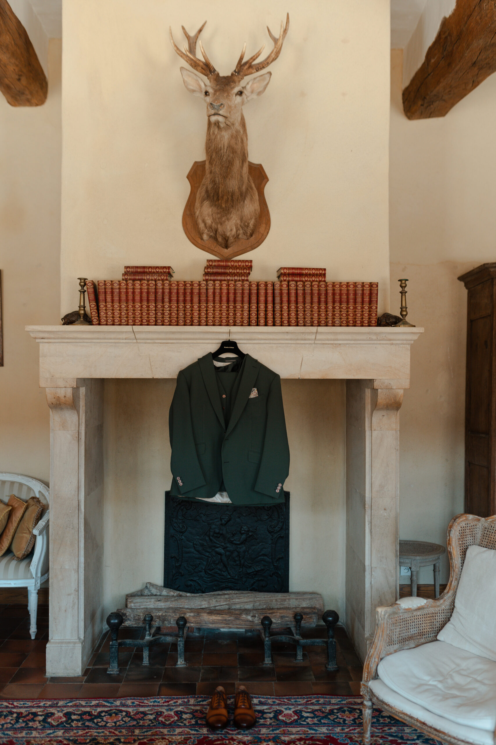 Costume vert du marié suspendu à une cheminée ancienne surmontée d'une tête de cerf au Château de Vaux.