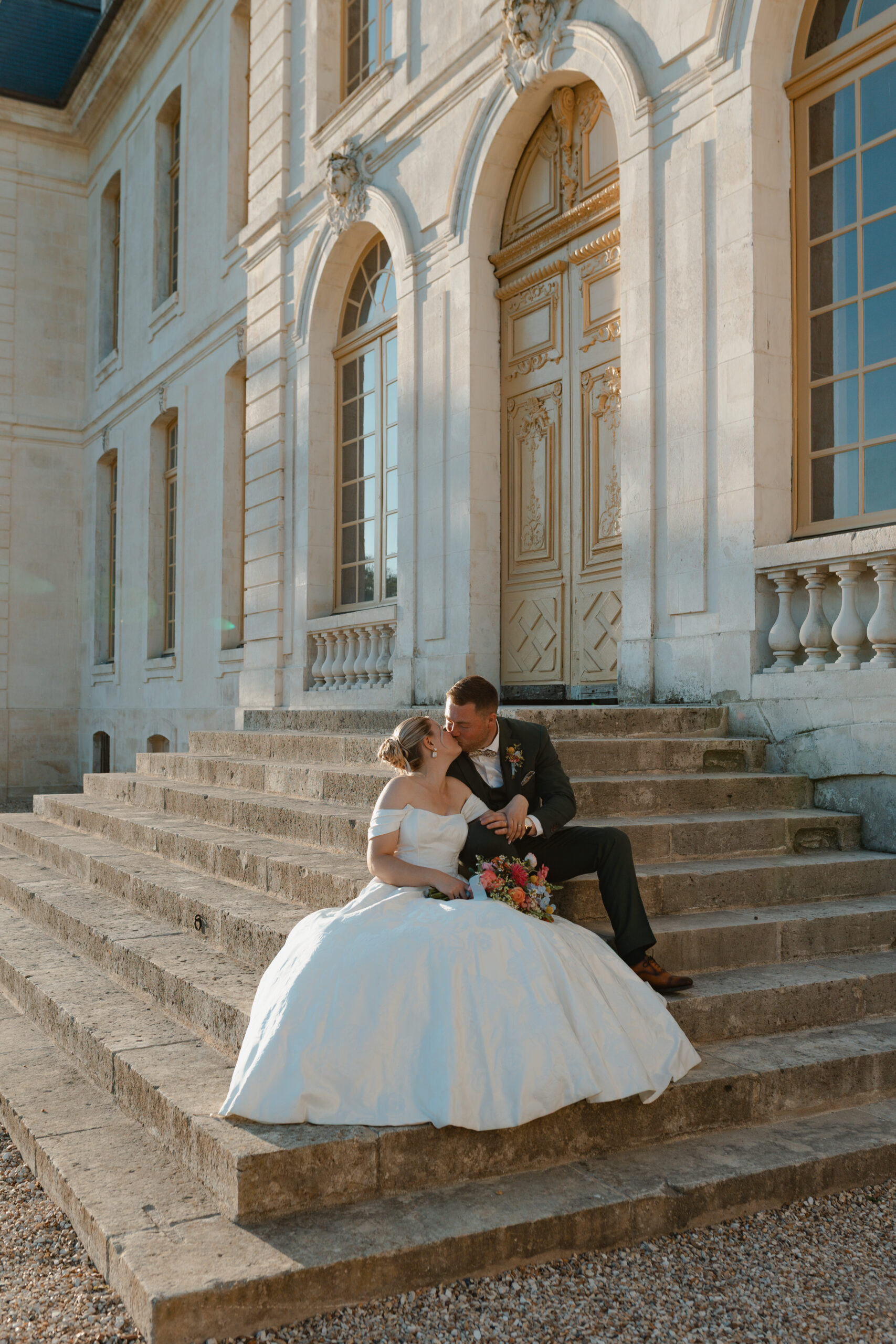 Couple de mariés s'embrassant sur les marches des escaliers devant la façade du Château de Vaux.