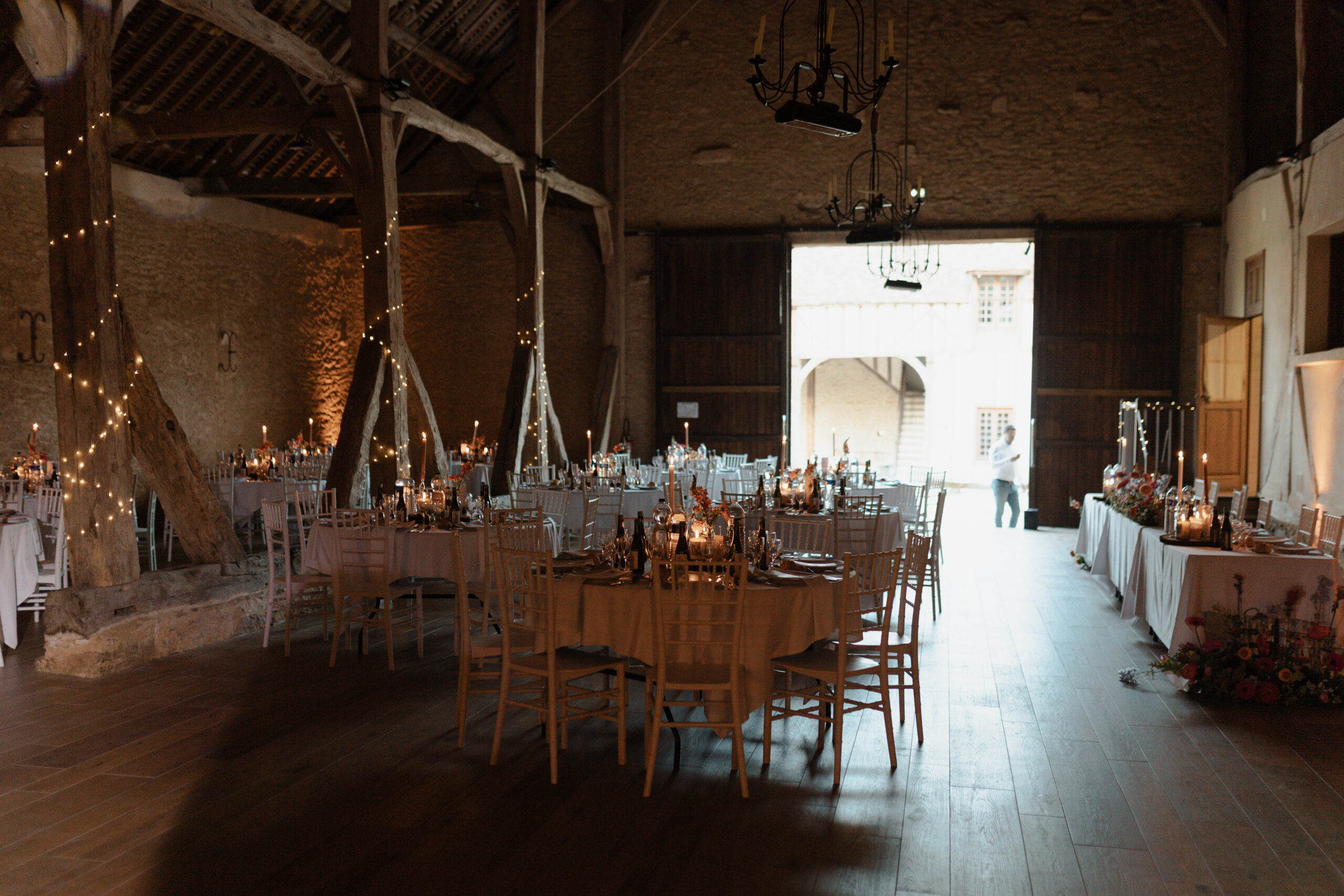Tables de réception installées dans la grange monumentale du Château de Vaux, ambiance tamisée.