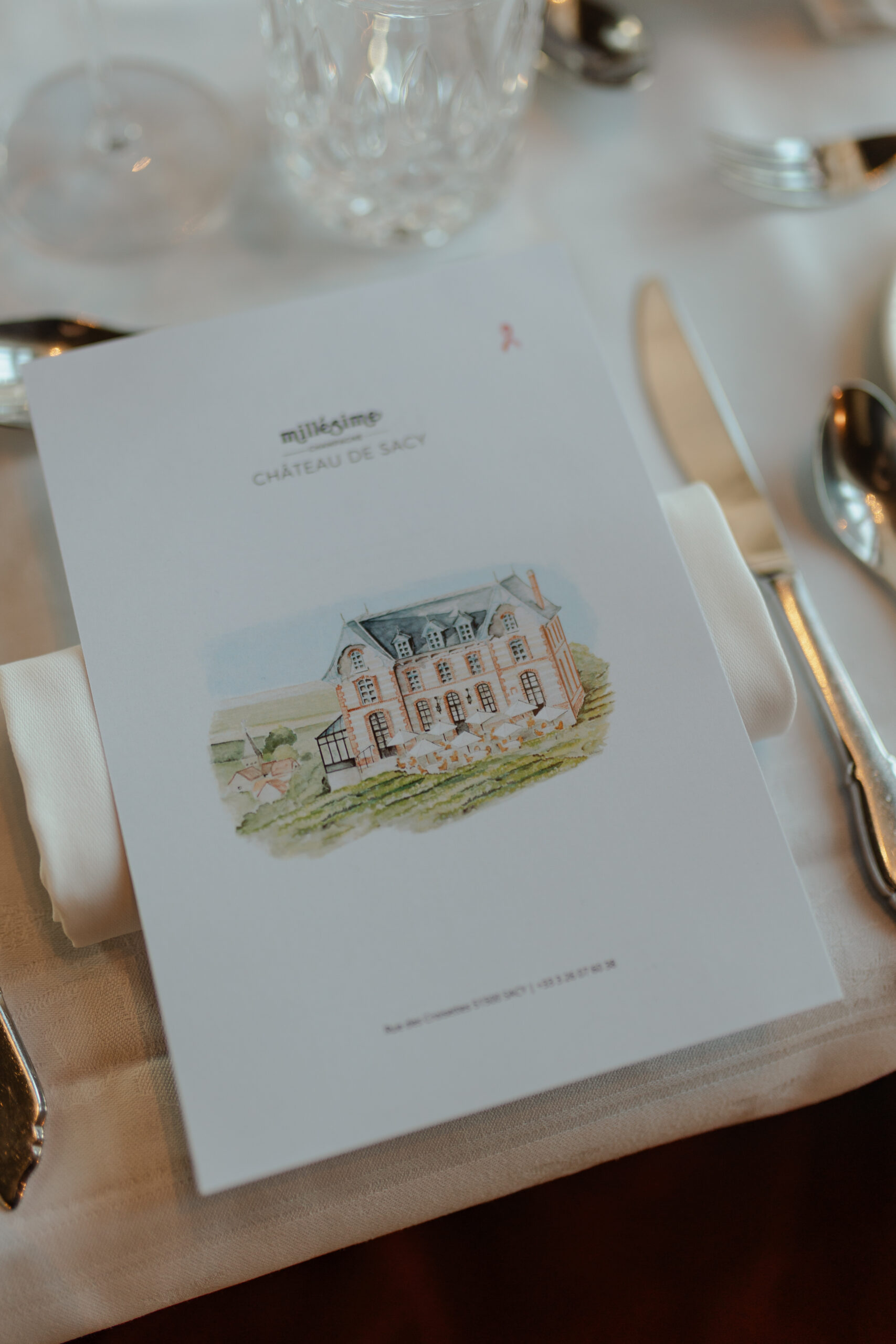 Gros plan sur un menu de mariage avec une illustration élégante du Château de Sacy. Détail de papeterie fine déposé sur une table dressée en Champagne.