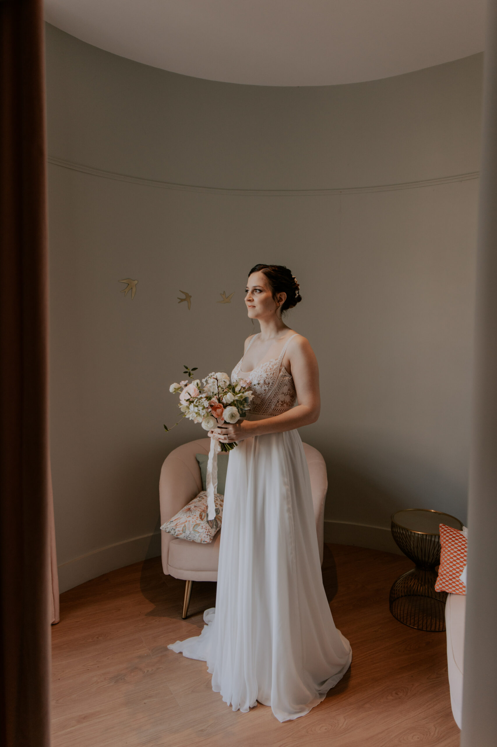 Portrait de la mariée avec son bouquet au centre de la tour du château. Vue de l'intérieur, regard tourné vers l'extérieur.