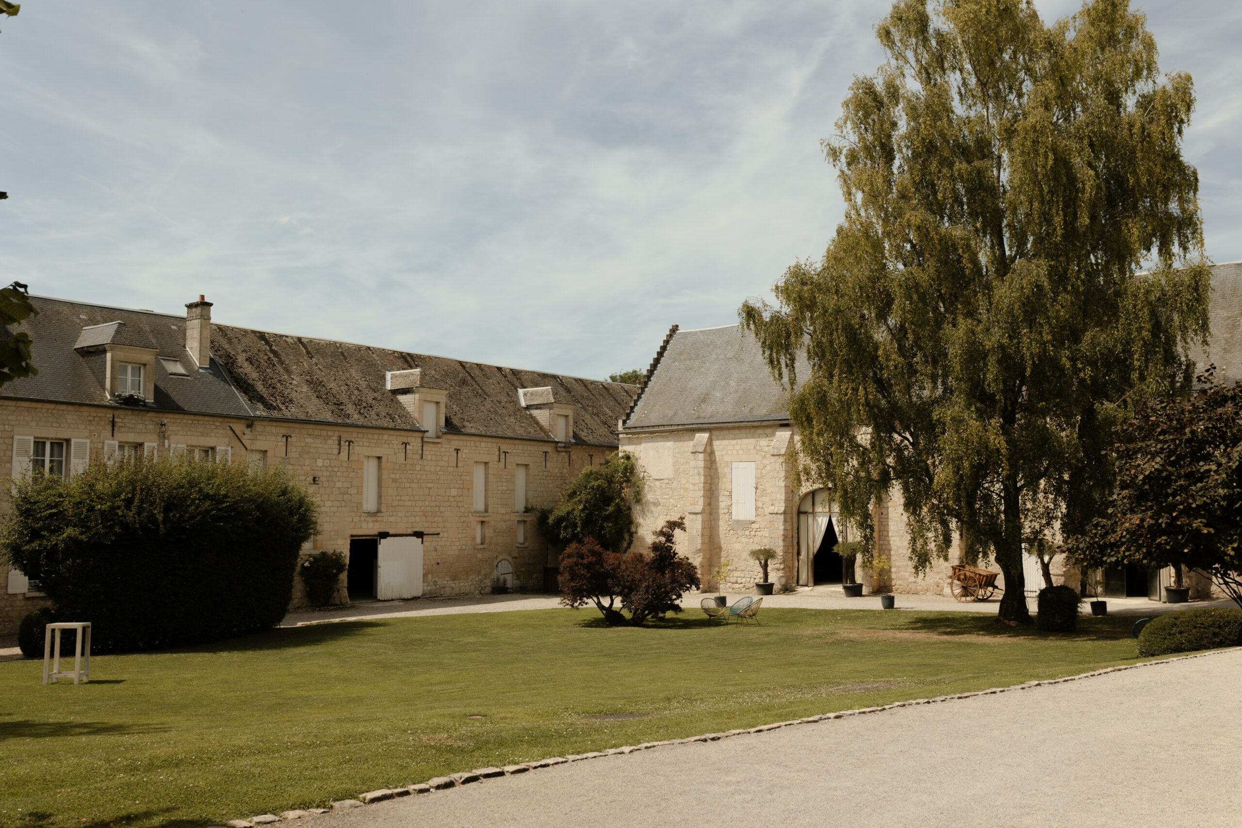Vue d'ensemble du domaine Les Pommerieux mettant en valeur les bâtisses en pierre sous le soleil d'été, domaine mariage Reims Champagne.