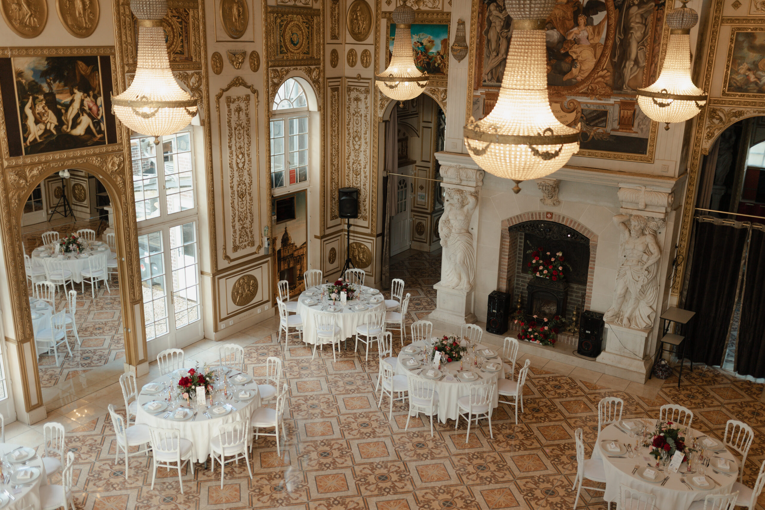 Salle de réception prise depuis la mezzanine, focus sur les lustres en cristal et les tables de mariage.
