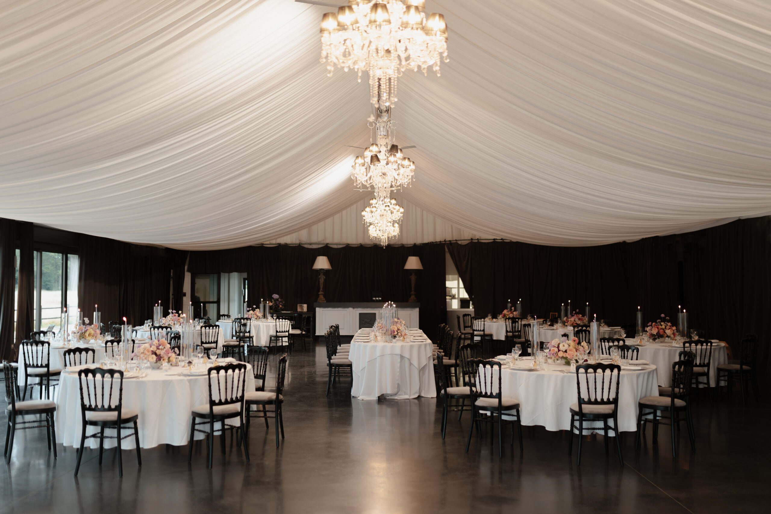 Réception de mariage dans l'orangeraie du Château du Faucon avec lustres, murs noirs et dalles cirées.