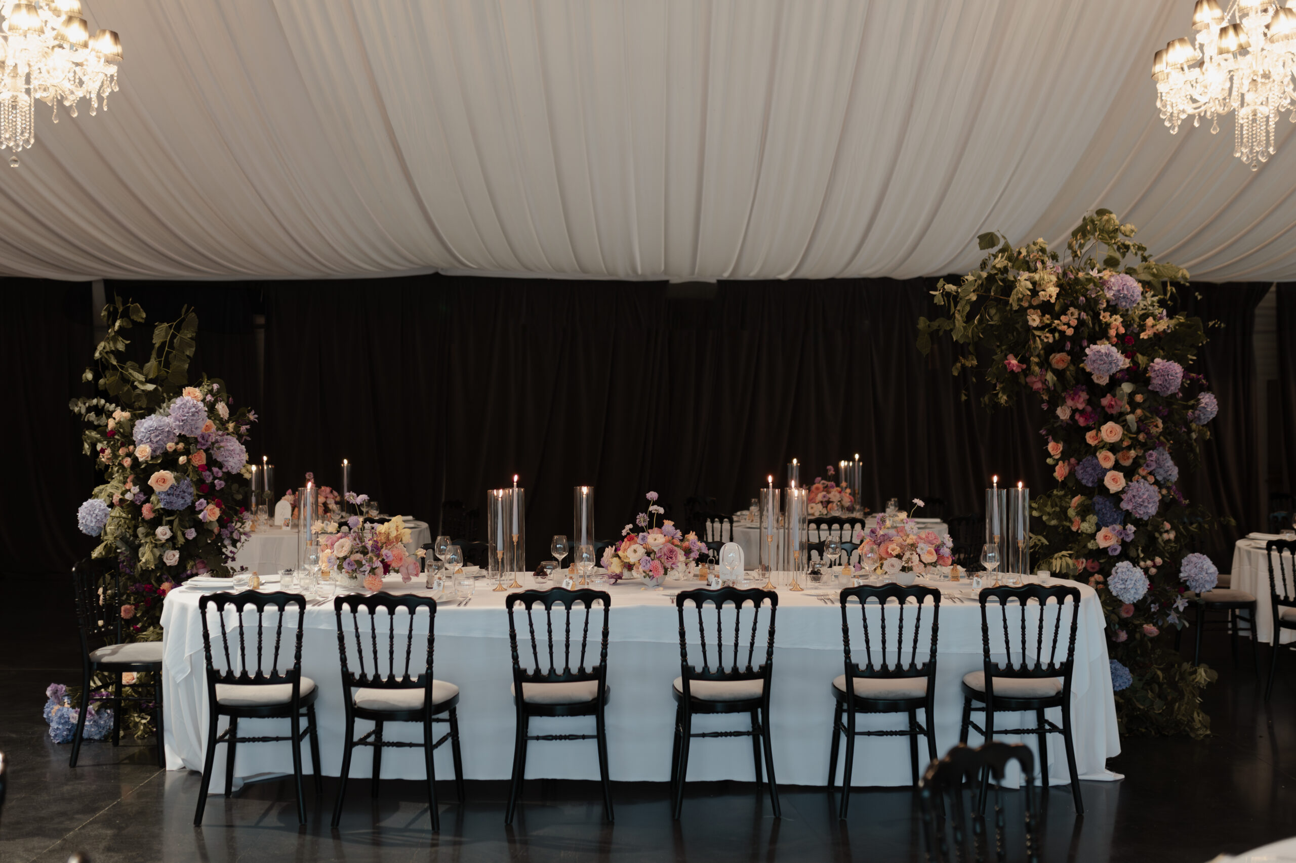 Table d'honneur décorée d'une arche asymétrique et de chandelles, thème pastel chic au Domaine du Château du Faucon.