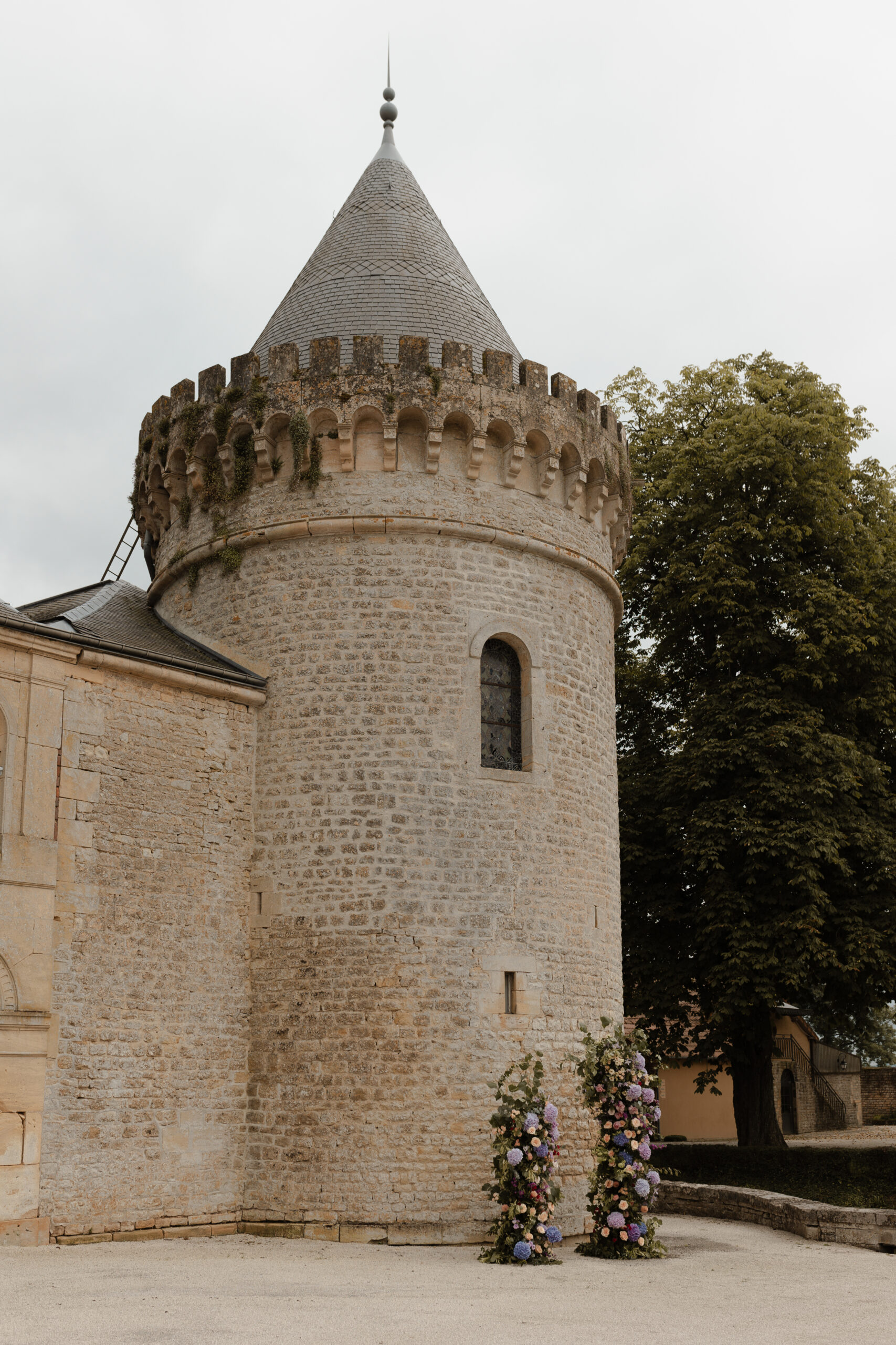 Tour droite du Château du Faucon avec arche florale asymétrique à sa base pour une cérémonie.