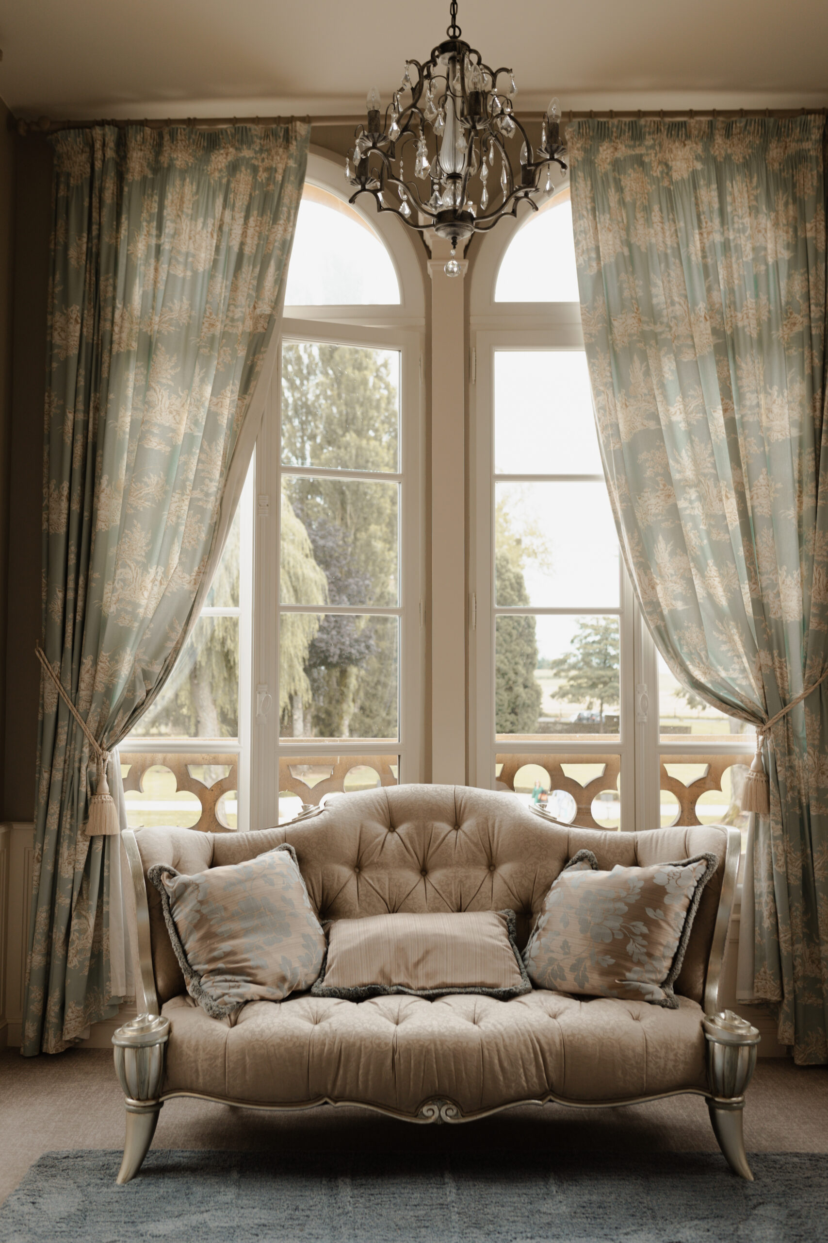 Chambre des mariés au Château du Faucon avec canapé d'époque, rideaux et vue sur la verdure.