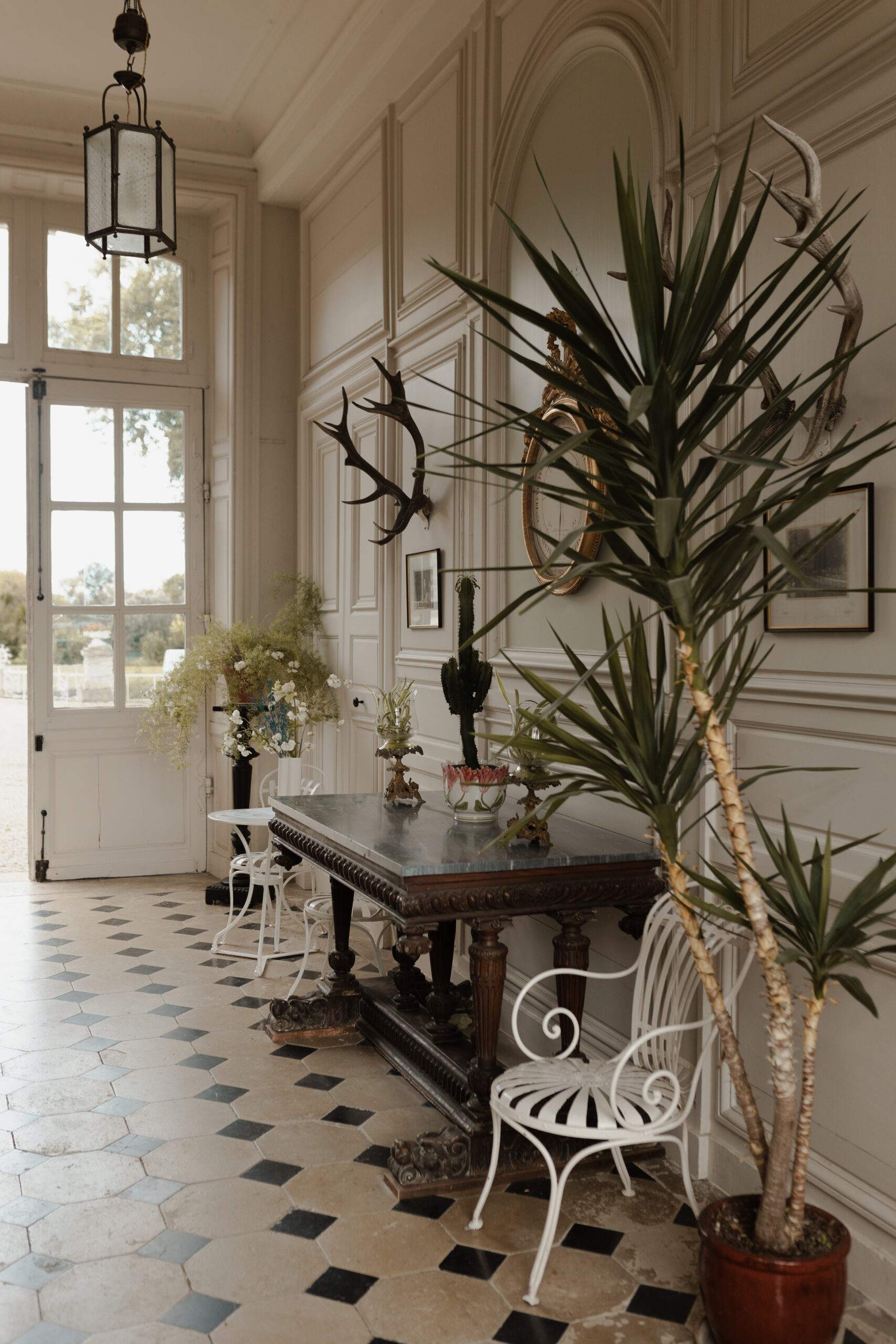 Vue du hall d'entrée du Château de Juvigny montrant les moulures, les plantes d'intérieur et le mobilier de prestige.