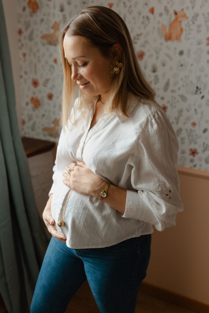 Portrait d'une future maman dans la chambre de bébé à Reims, regard tendre porté sur son ventre arrondi.