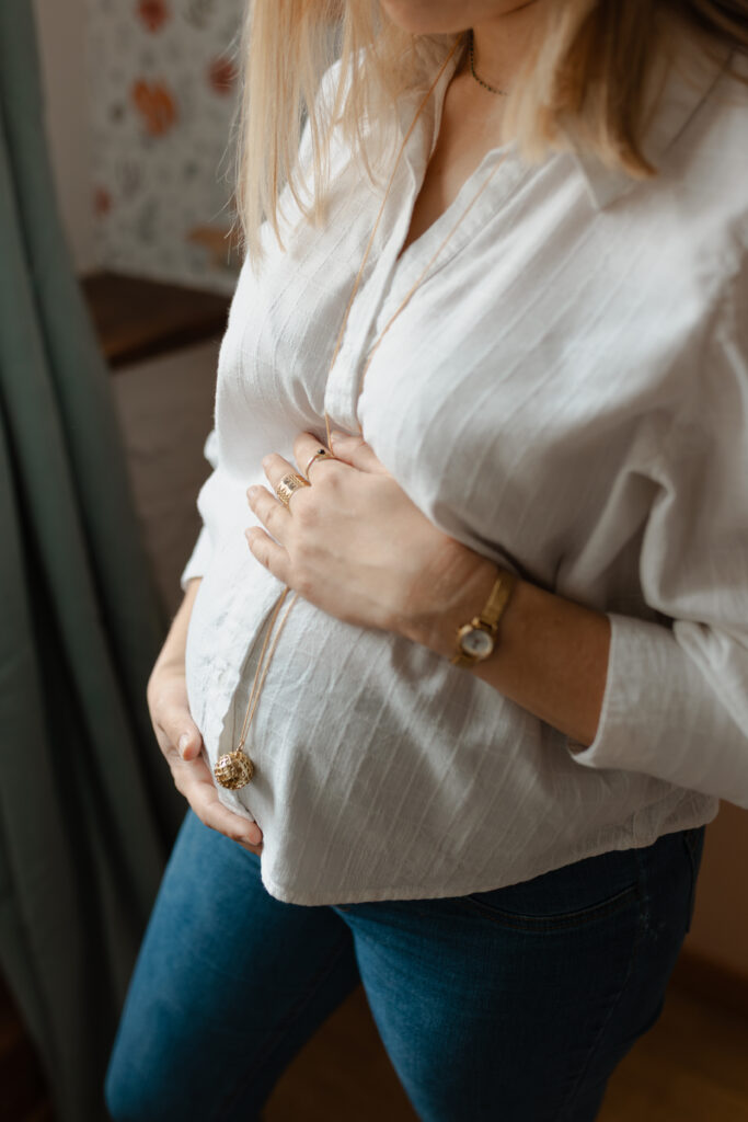 Gros plan sur le ventre de grossesse d'une maman, mains posées dessus et dessous pour souligner l'arrondi. Séance photo grossesse à domicile à Reims.