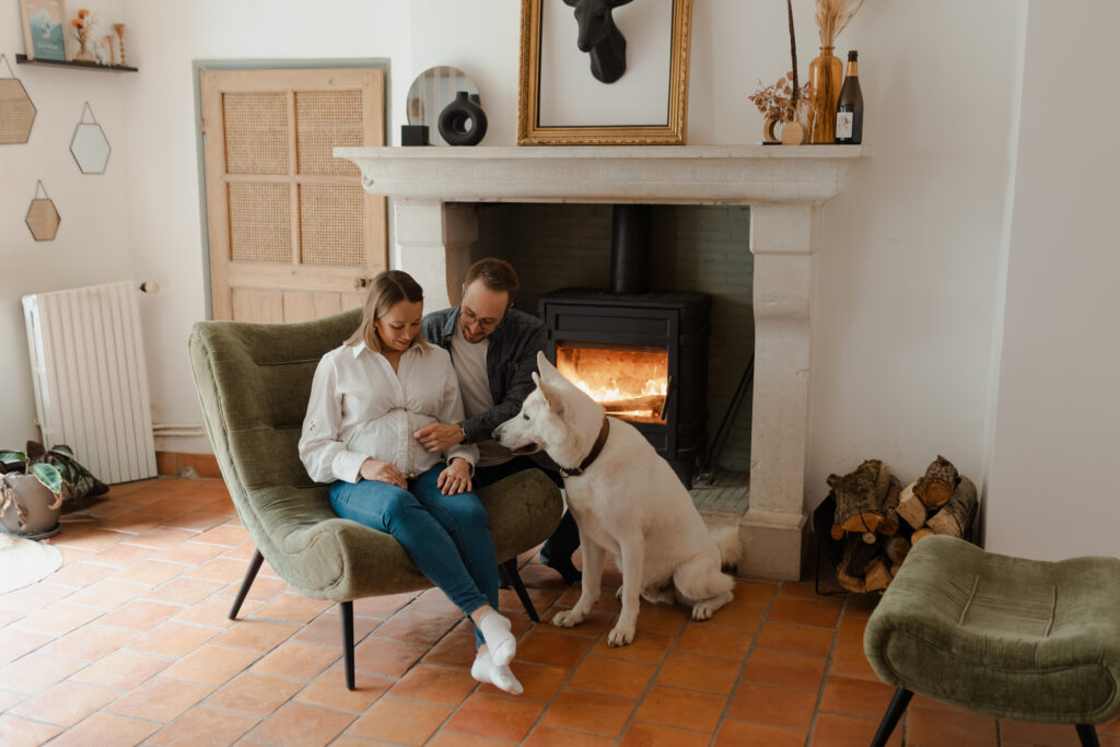 Plan large d'un couple et leur chien regardant ensemble le ventre de grossesse dans un salon cosy.
